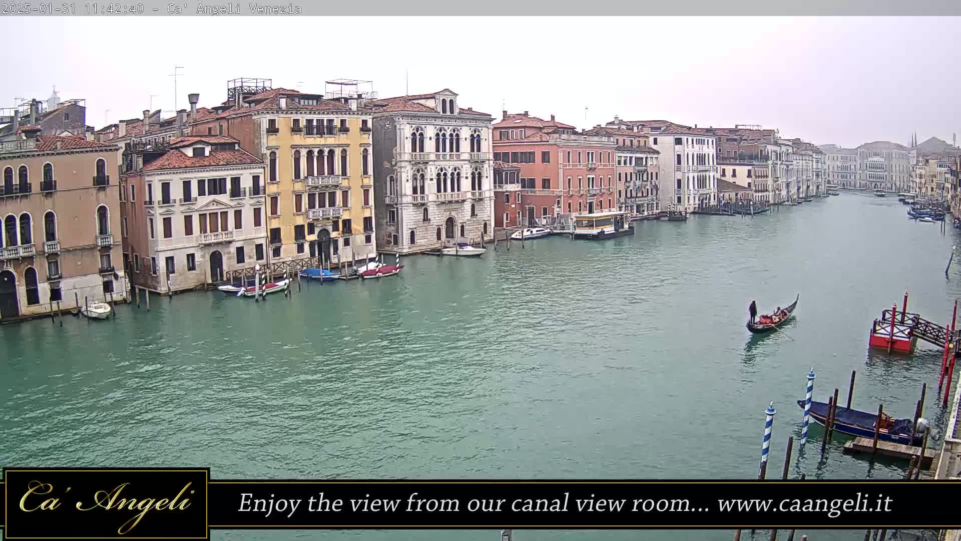 A gondola floats on a wide canal in Venice, Italy, under an overcast sky, flanked by numerous buildings lining the waterway.