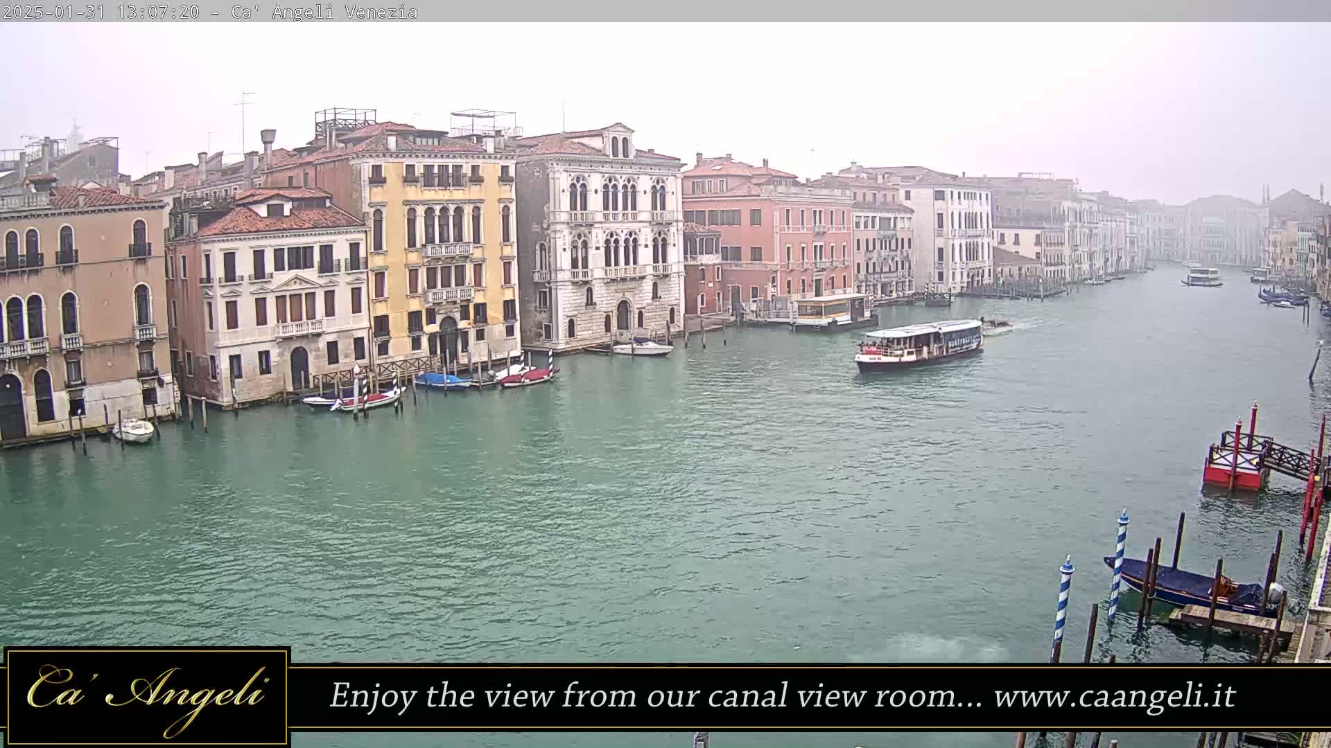 A foggy view of a canal in Venice, Italy, shows several buildings lining the waterway and several boats on the water.