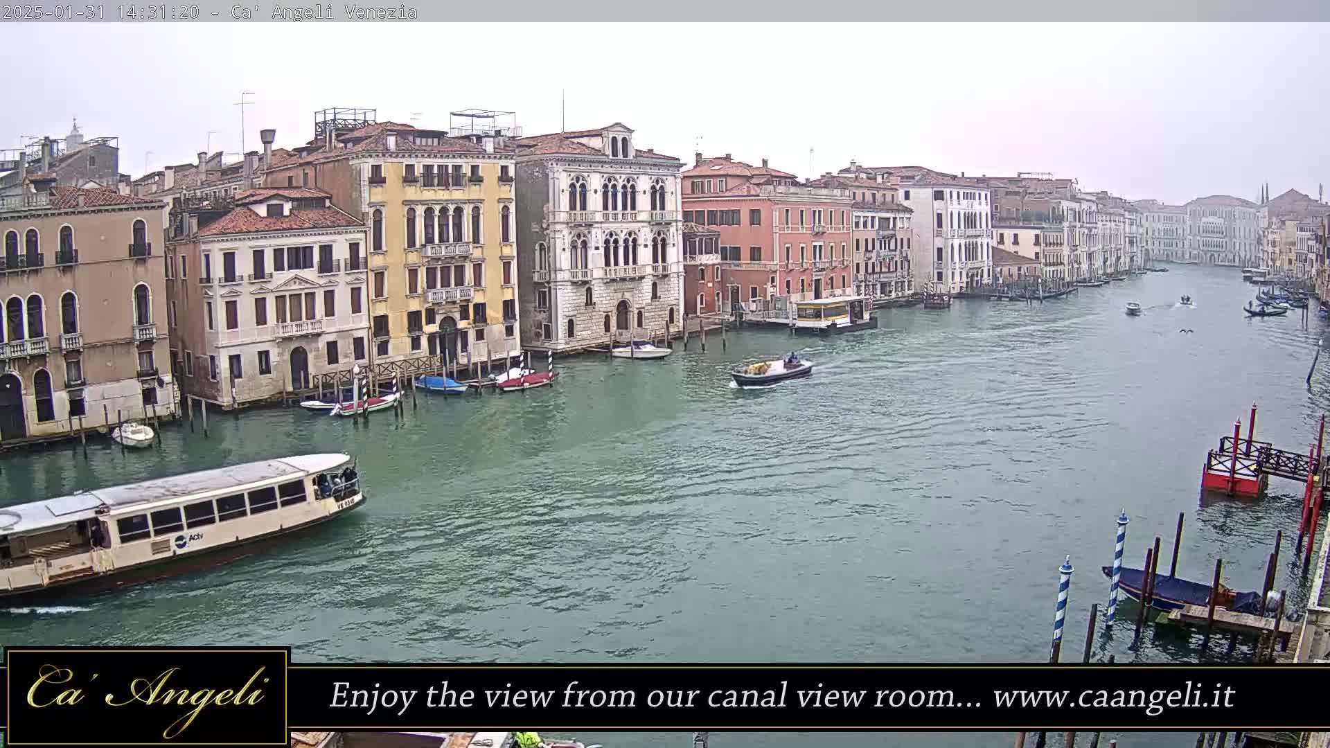 A wide shot of a canal in Venice, Italy, on an overcast day, shows numerous boats and buildings lining the waterway.