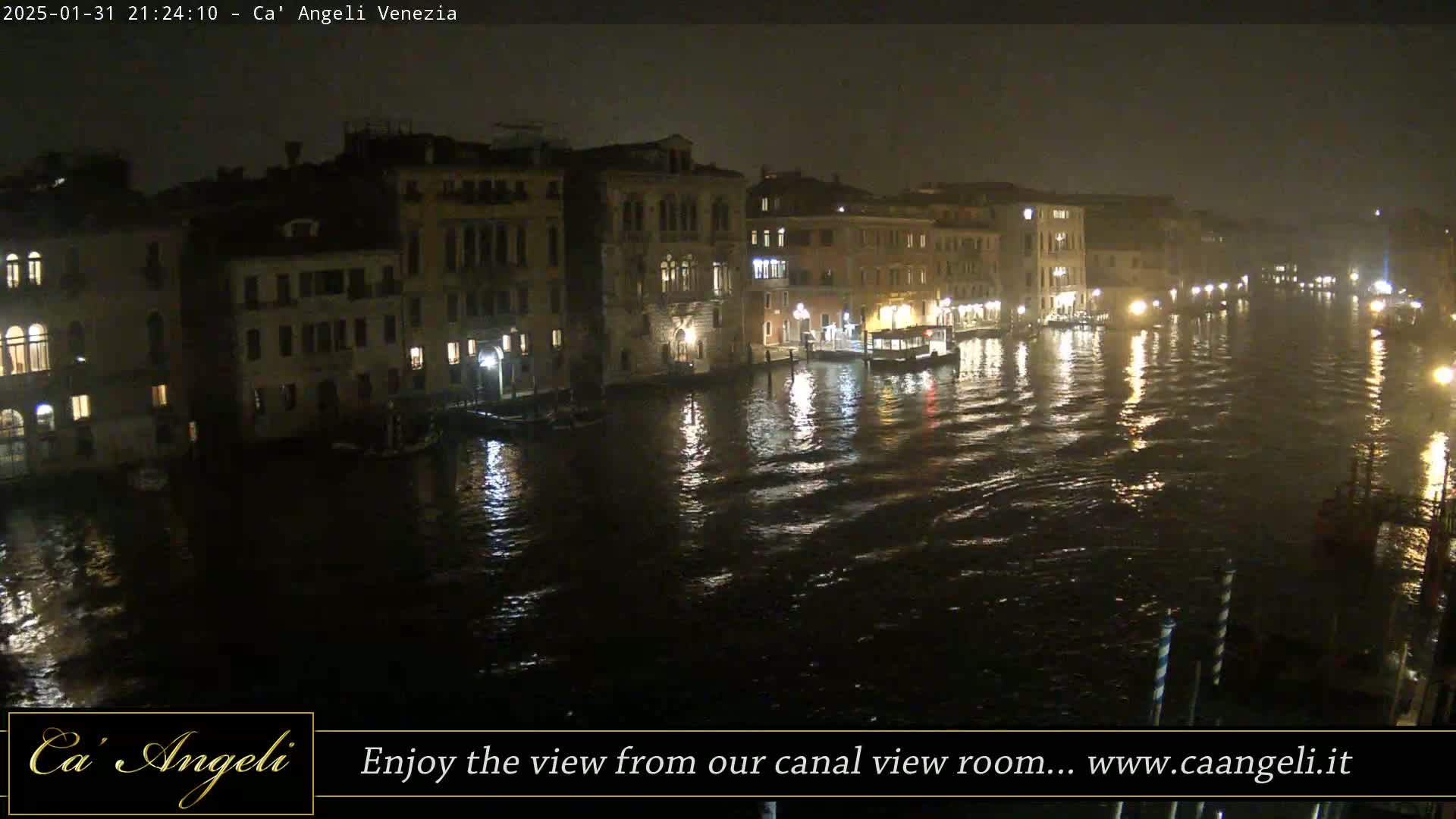 A nighttime view of a canal in Venice, with illuminated buildings lining the waterway, under slightly overcast skies.