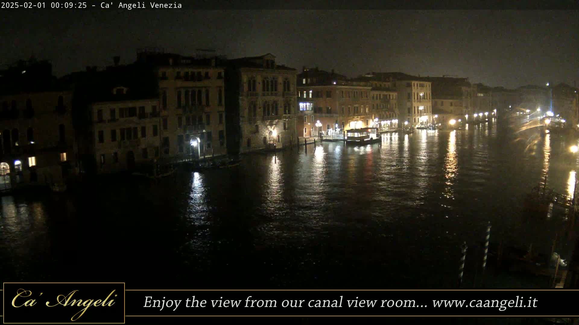 A nighttime view of a canal in Venice, Italy, shows dark buildings lining the waterway, with lights reflecting on the water's surface.
