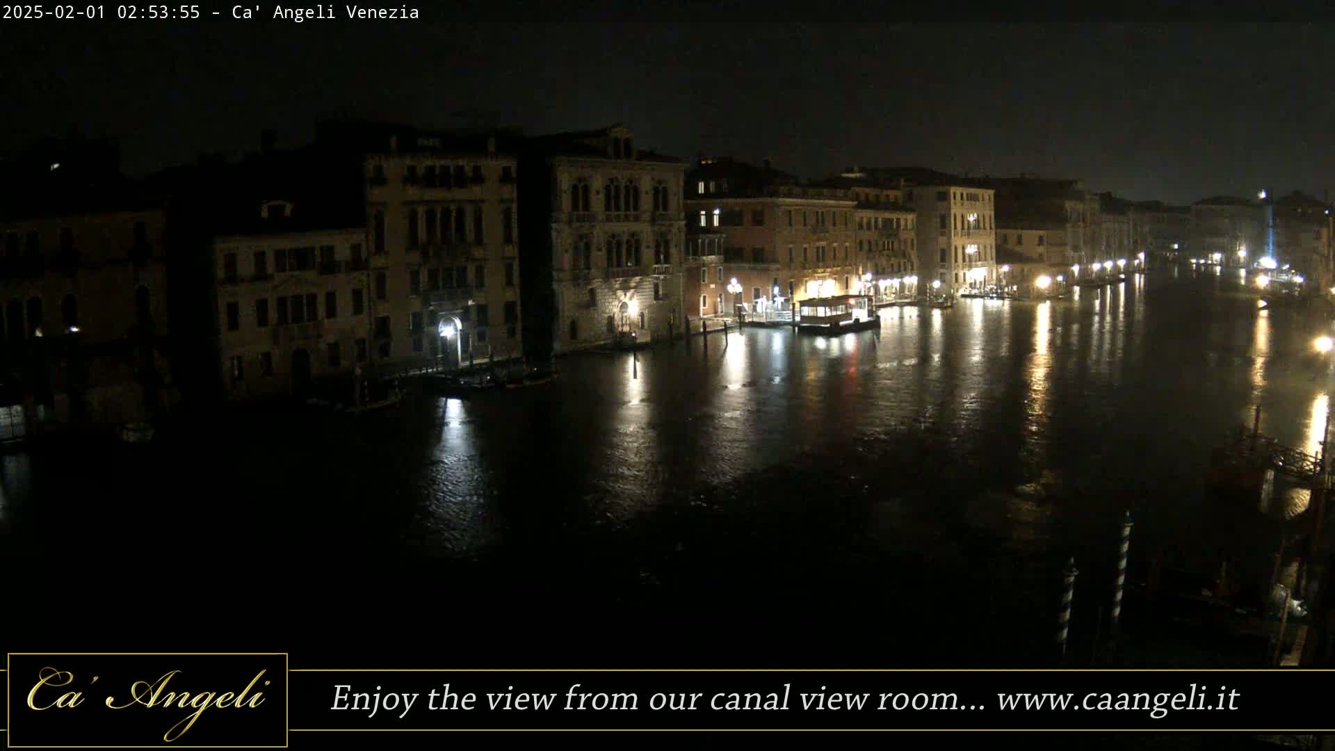 A nighttime view of a canal in Venice, showing illuminated buildings lining the waterway, with calm water reflecting the lights.