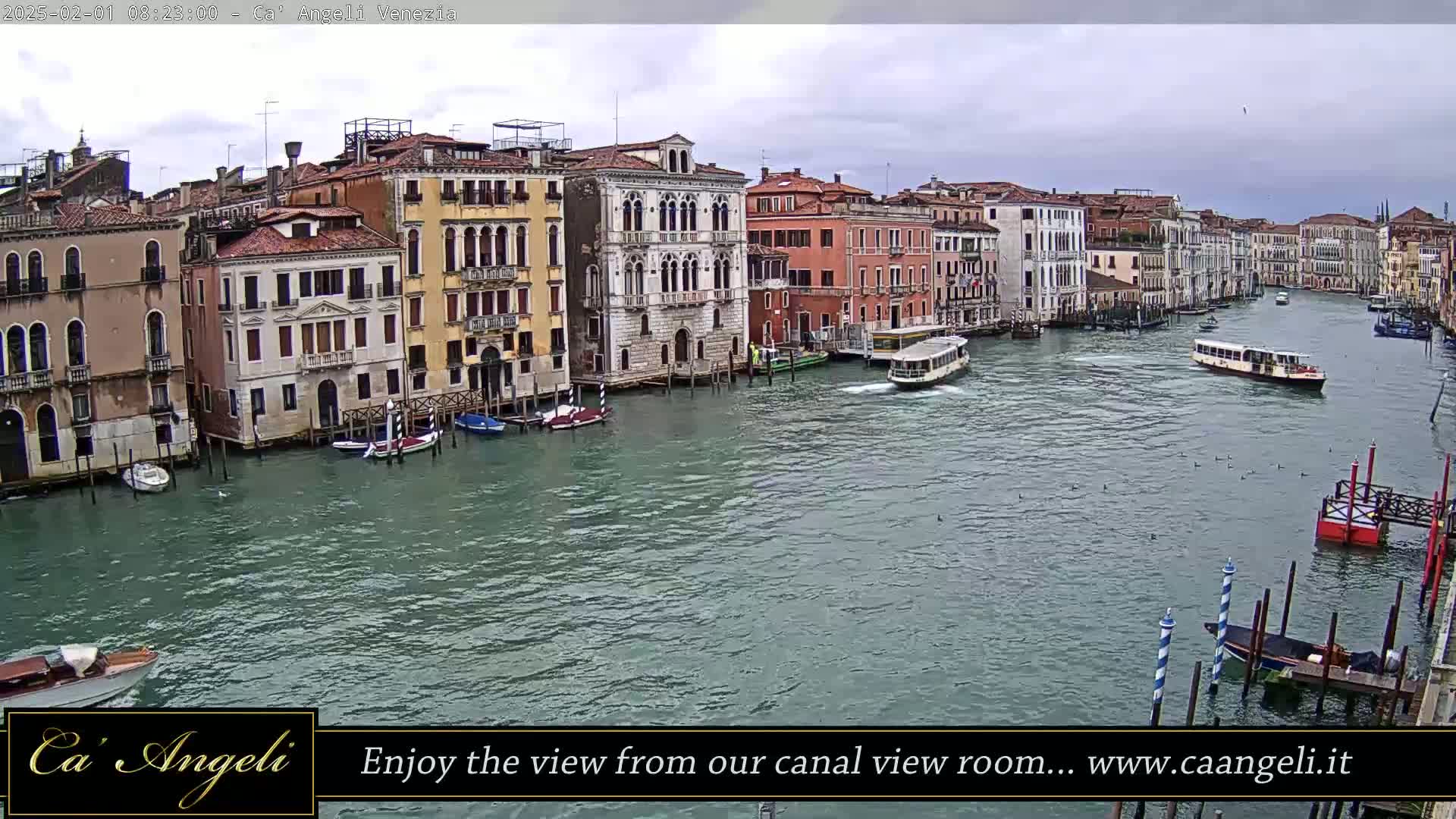 A wide shot of a canal in Venice on an overcast day, showing several boats and numerous buildings lining the waterway.
