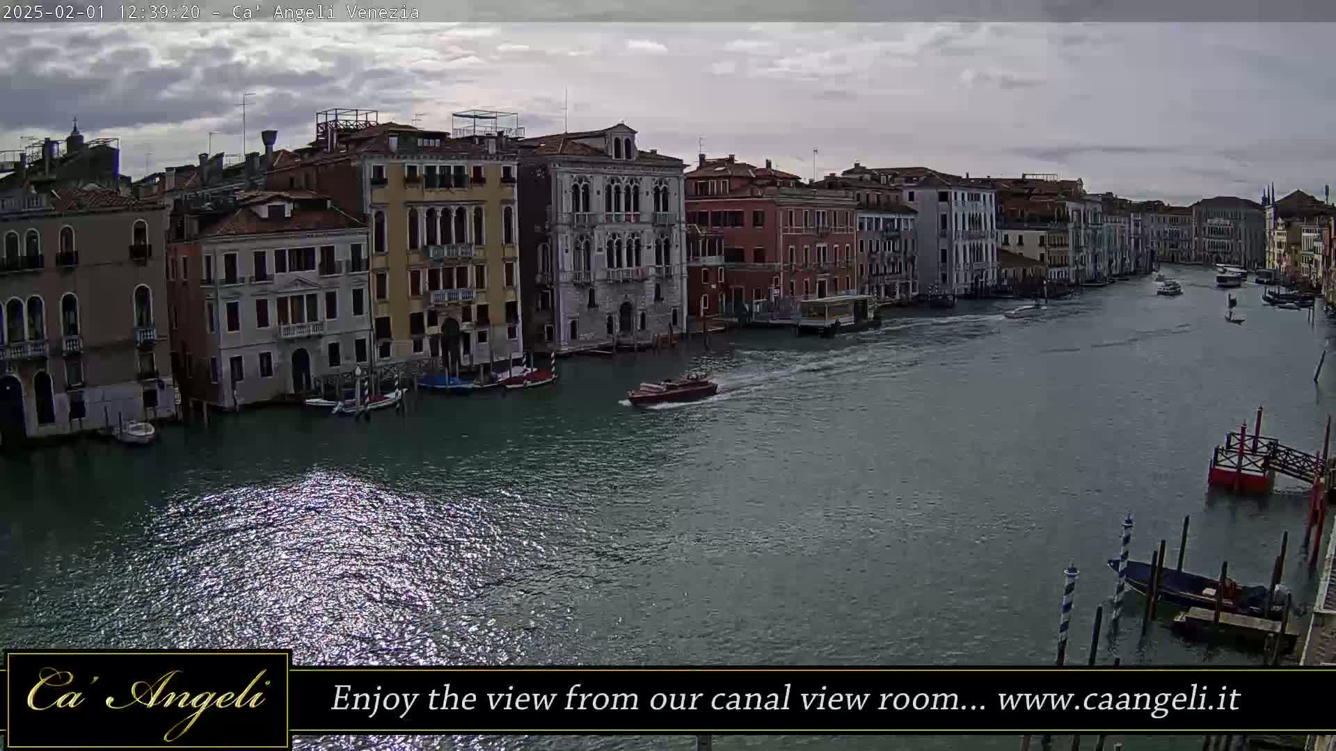 A canal in Venice, under a cloudy sky, is filled with boats passing by colorful buildings.