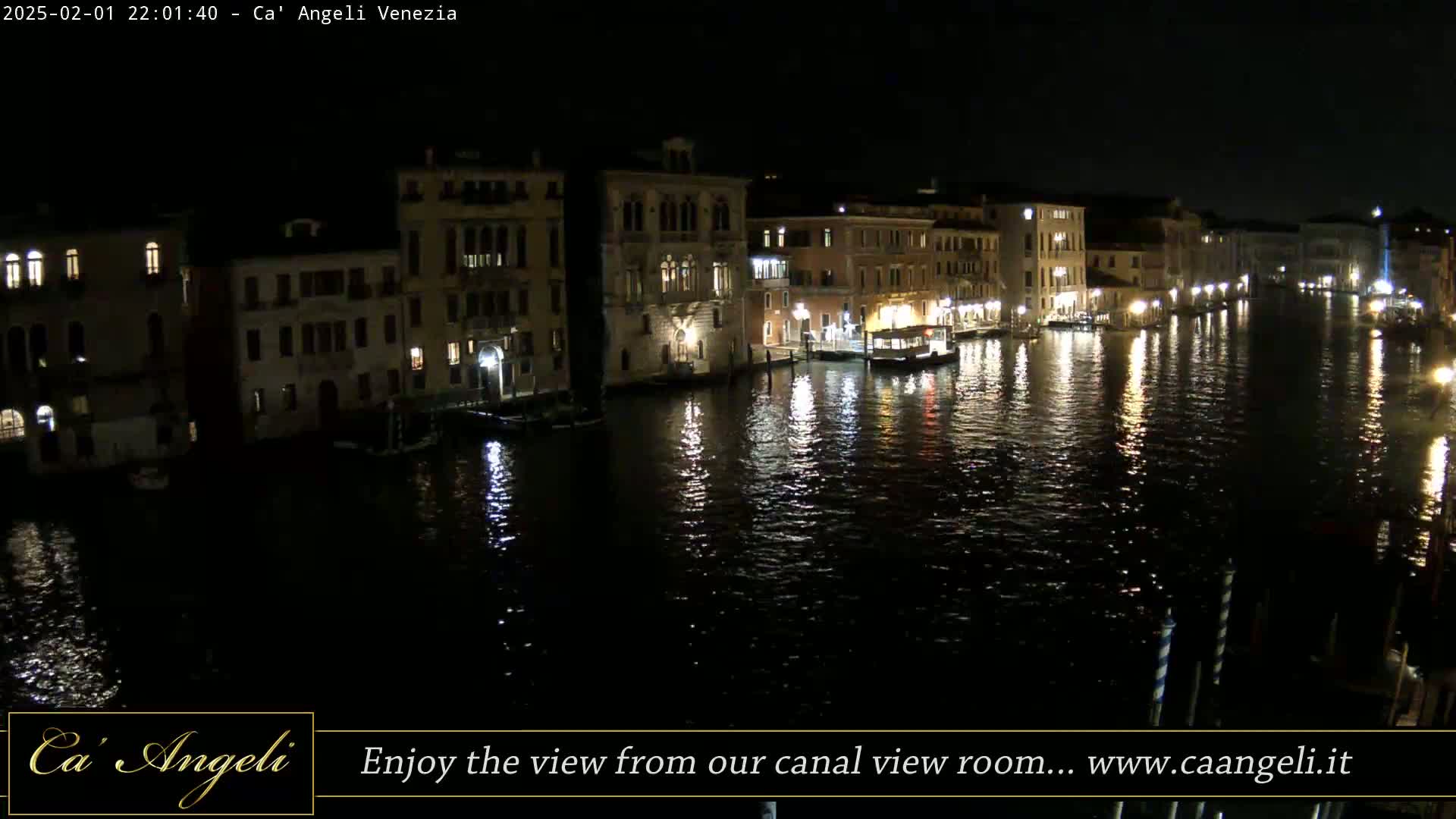 A nighttime view of a canal in Venice, lined with illuminated buildings and boats, under a dark sky.