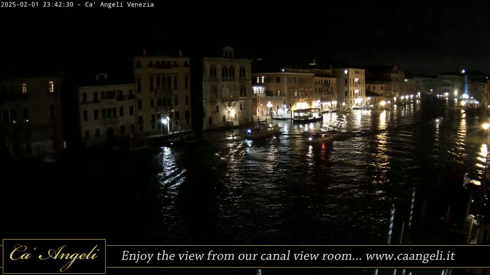 A nighttime view of a canal in Venice, with dark buildings lining the water's edge and several boats on the water.