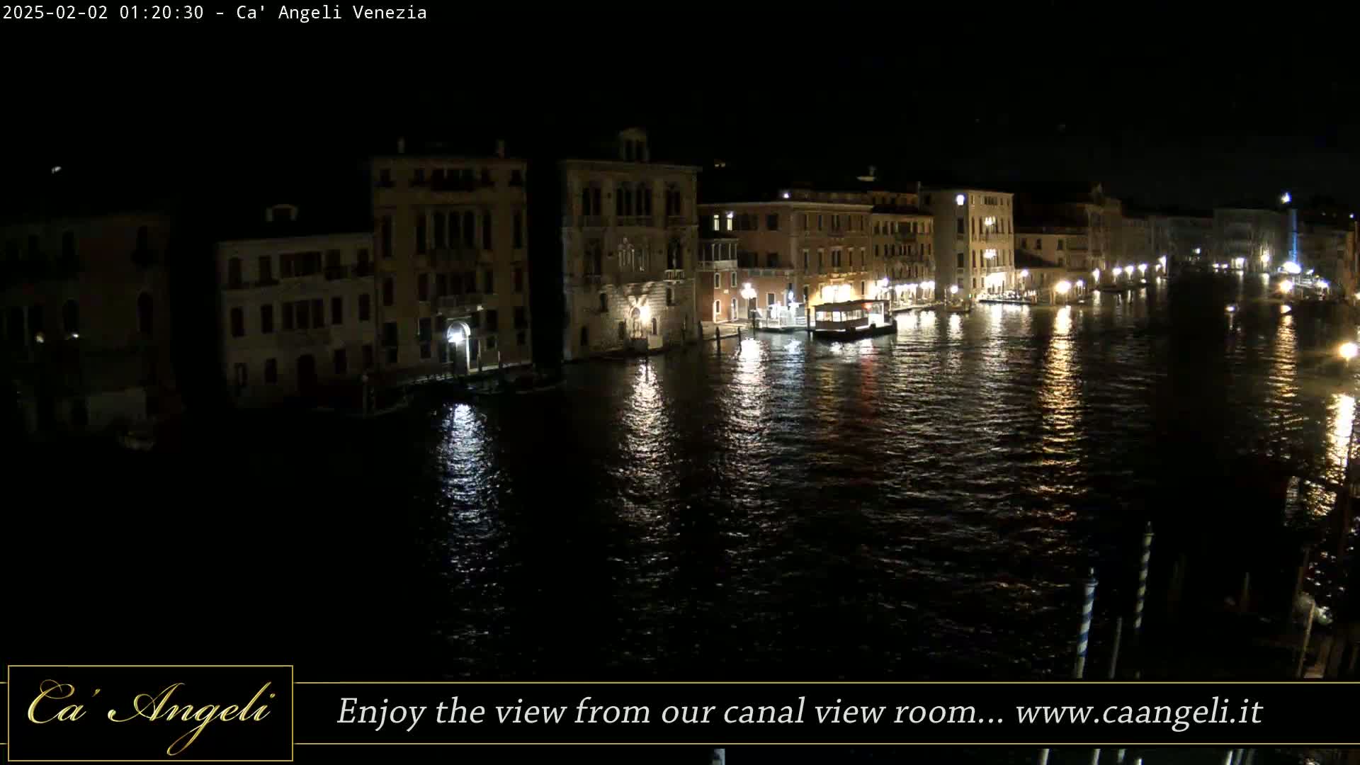 A nighttime view of a canal in Venice, with illuminated buildings lining its banks and a boat on the water.