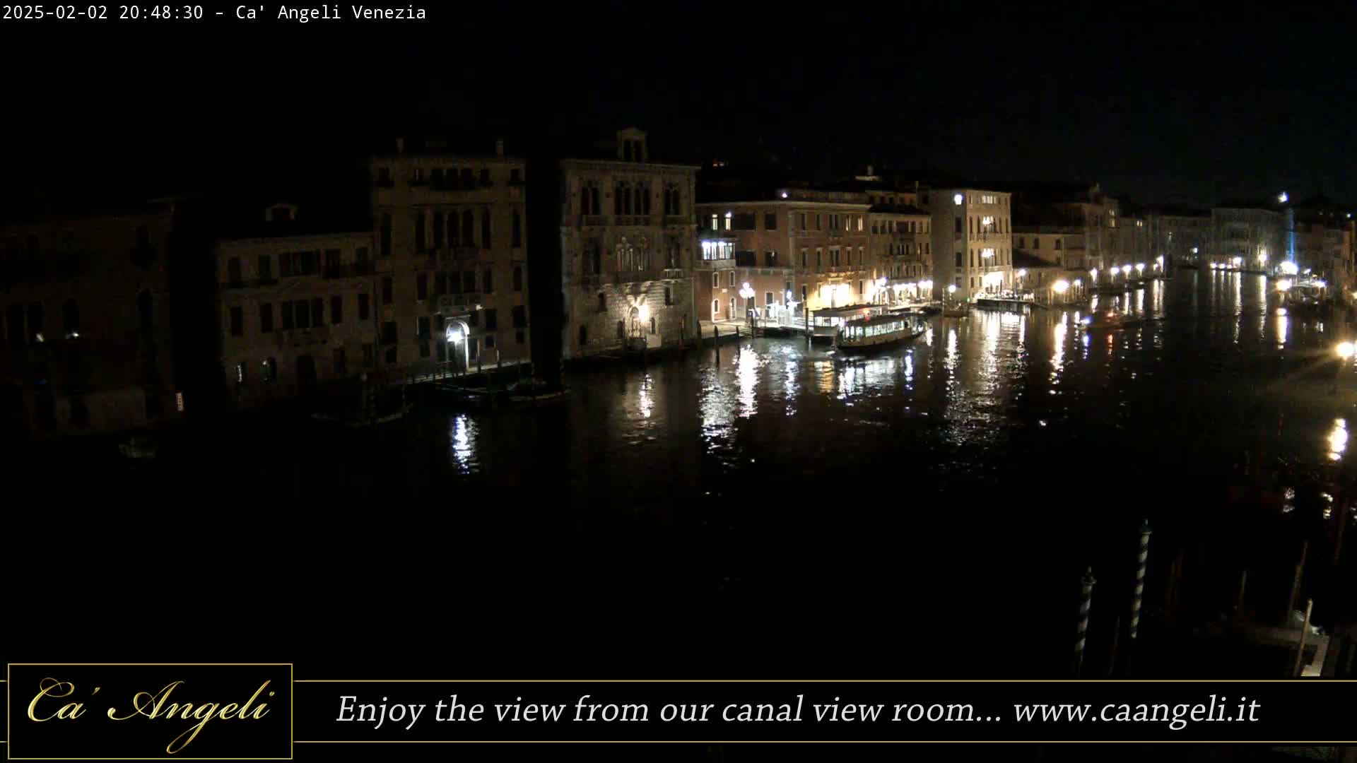 A nighttime view of a canal in Venice, with illuminated buildings lining the waterway and a boat visible on the water.