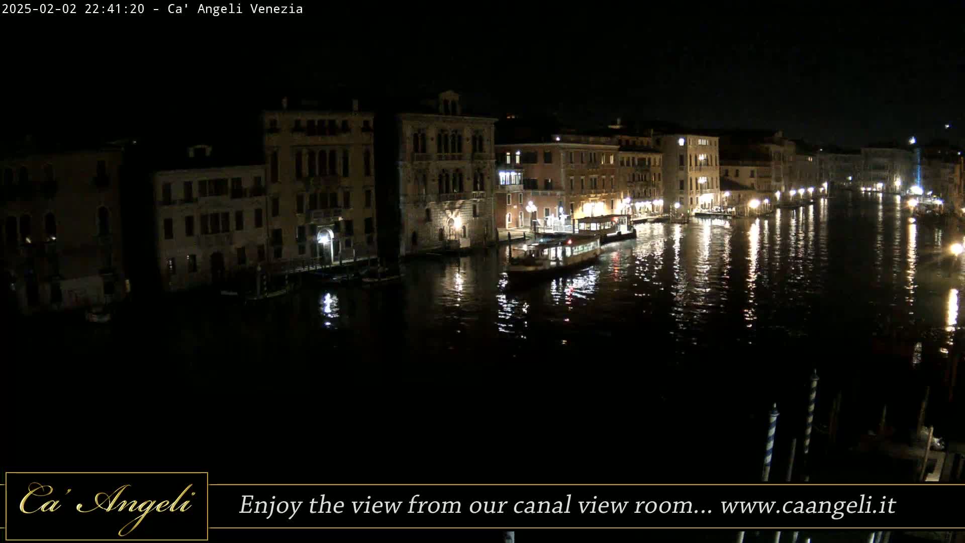 A nighttime view of a canal in Venice, with illuminated buildings lining the waterway and a boat on the water.