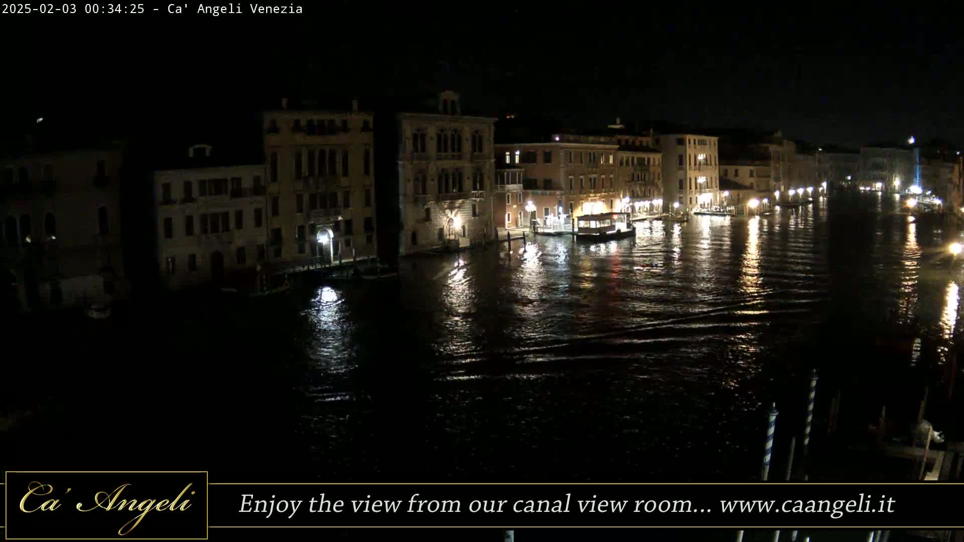 Nighttime view of a canal in Venice, with illuminated buildings lining the waterway and several boats moored along the banks.