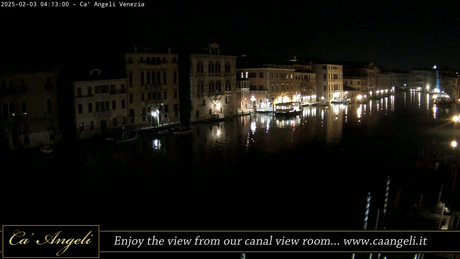 A nighttime view of a canal in Venice, lined with illuminated buildings, reflecting in the dark water.