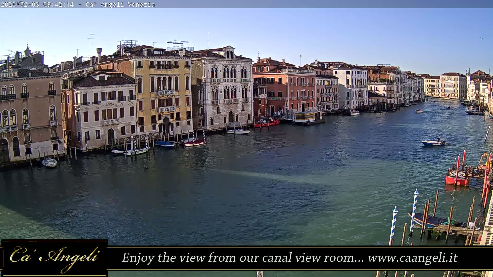 A sunny day in Venice shows a wide canal with numerous boats and historic buildings lining the waterfront.