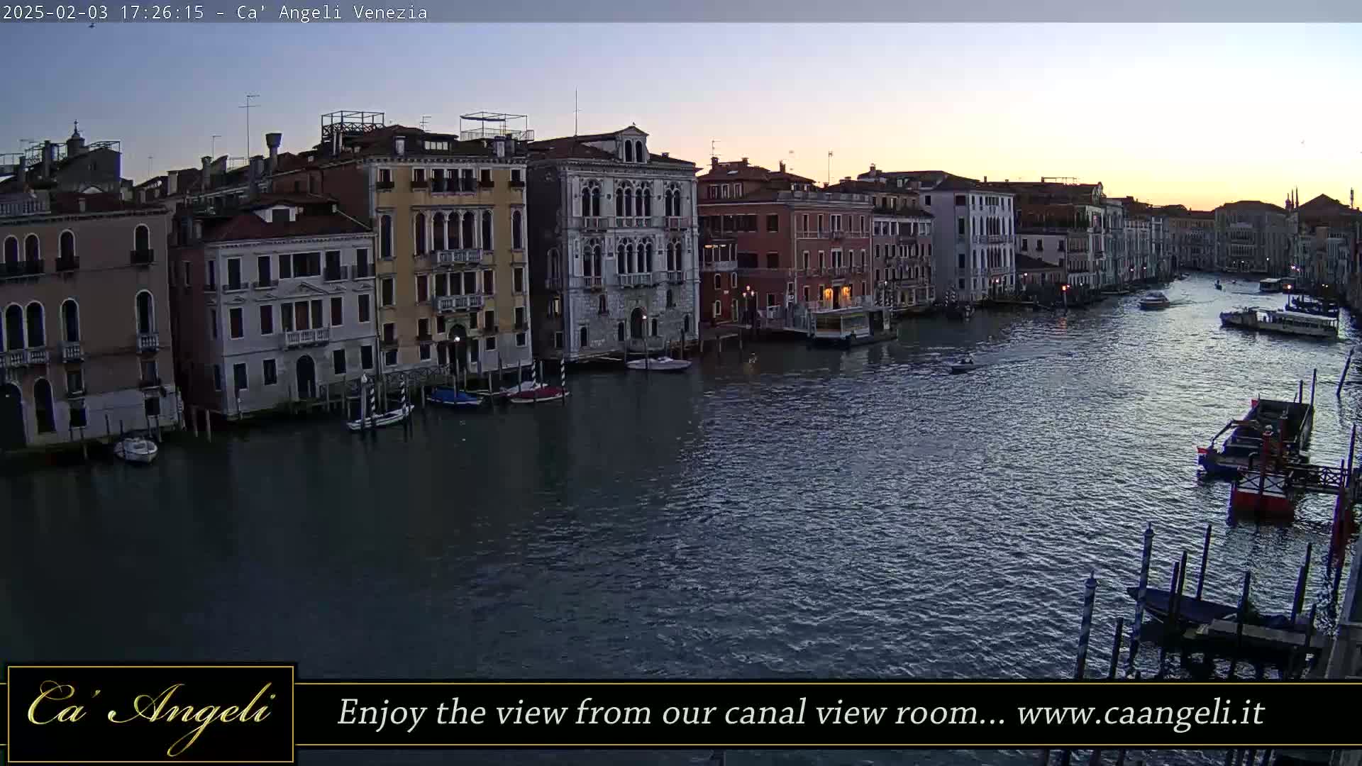 A twilight view of a canal in Venice, showing several buildings along its banks and various boats on the water.