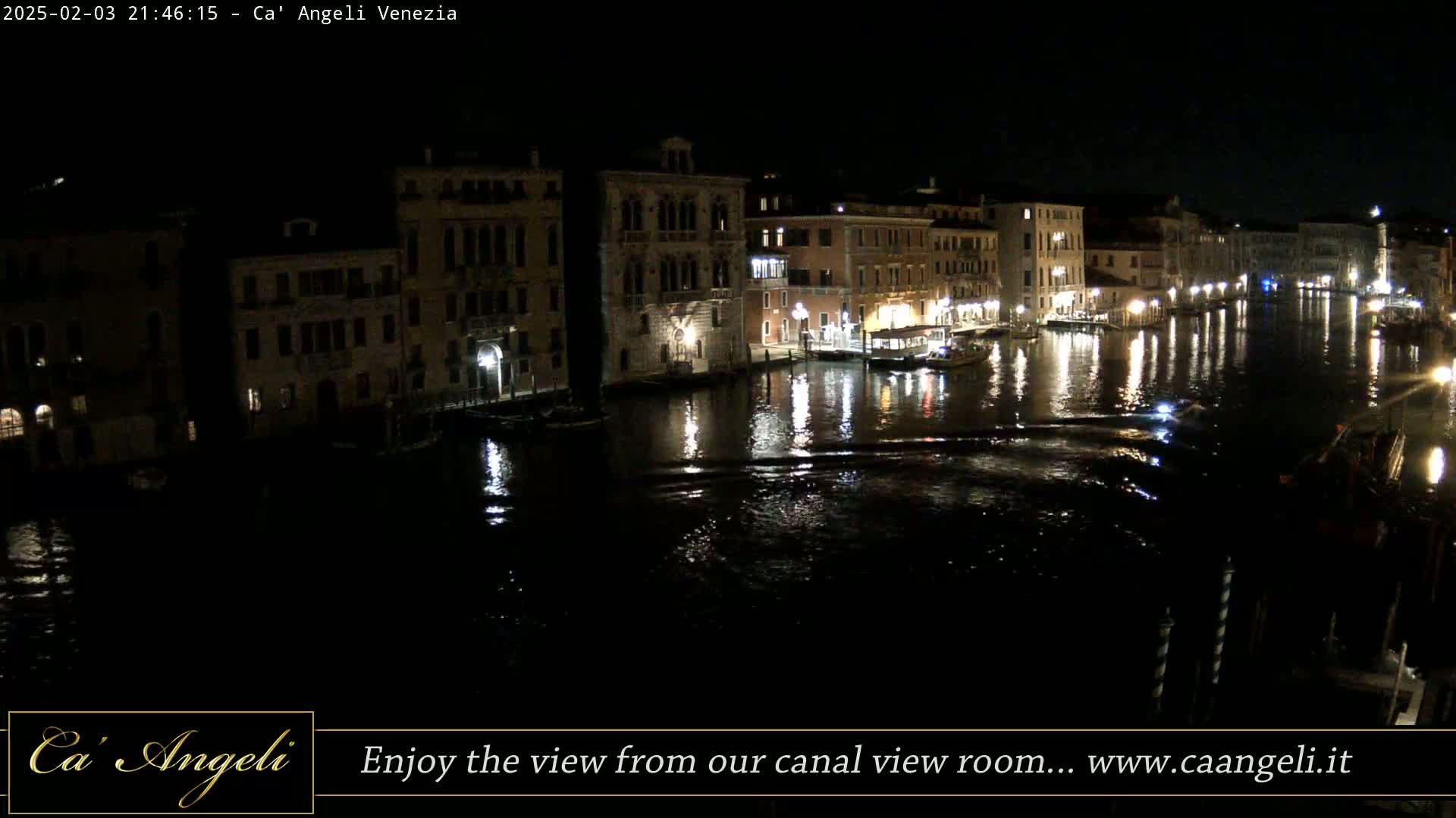 A nighttime view of a canal in Venice, Italy, shows dark buildings lit by streetlights and reflecting in the calm water.