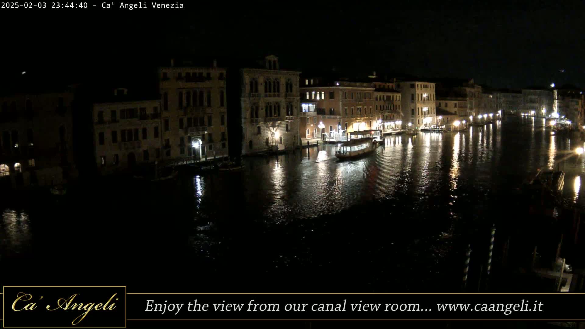 A nighttime view of a canal in Venice, showing illuminated buildings and boats on the water.