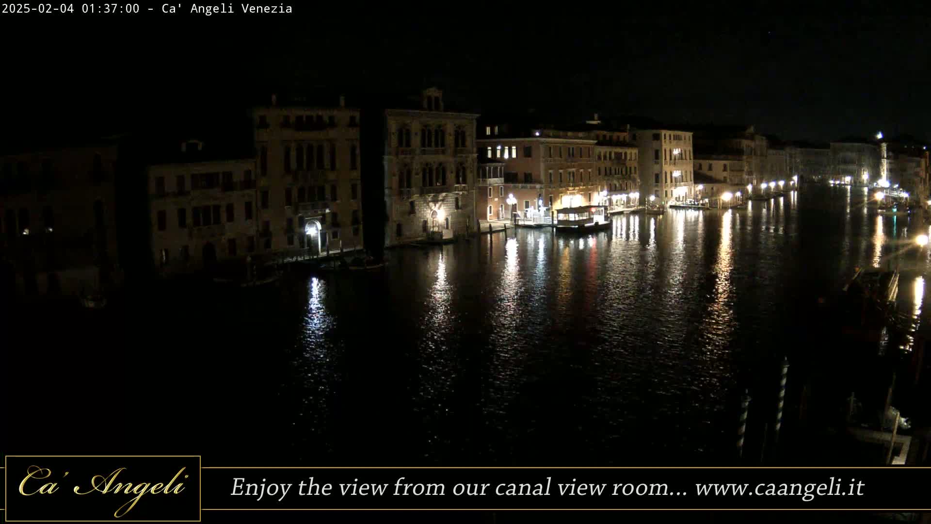 At night, illuminated buildings line a calm canal reflecting lights on its dark water.