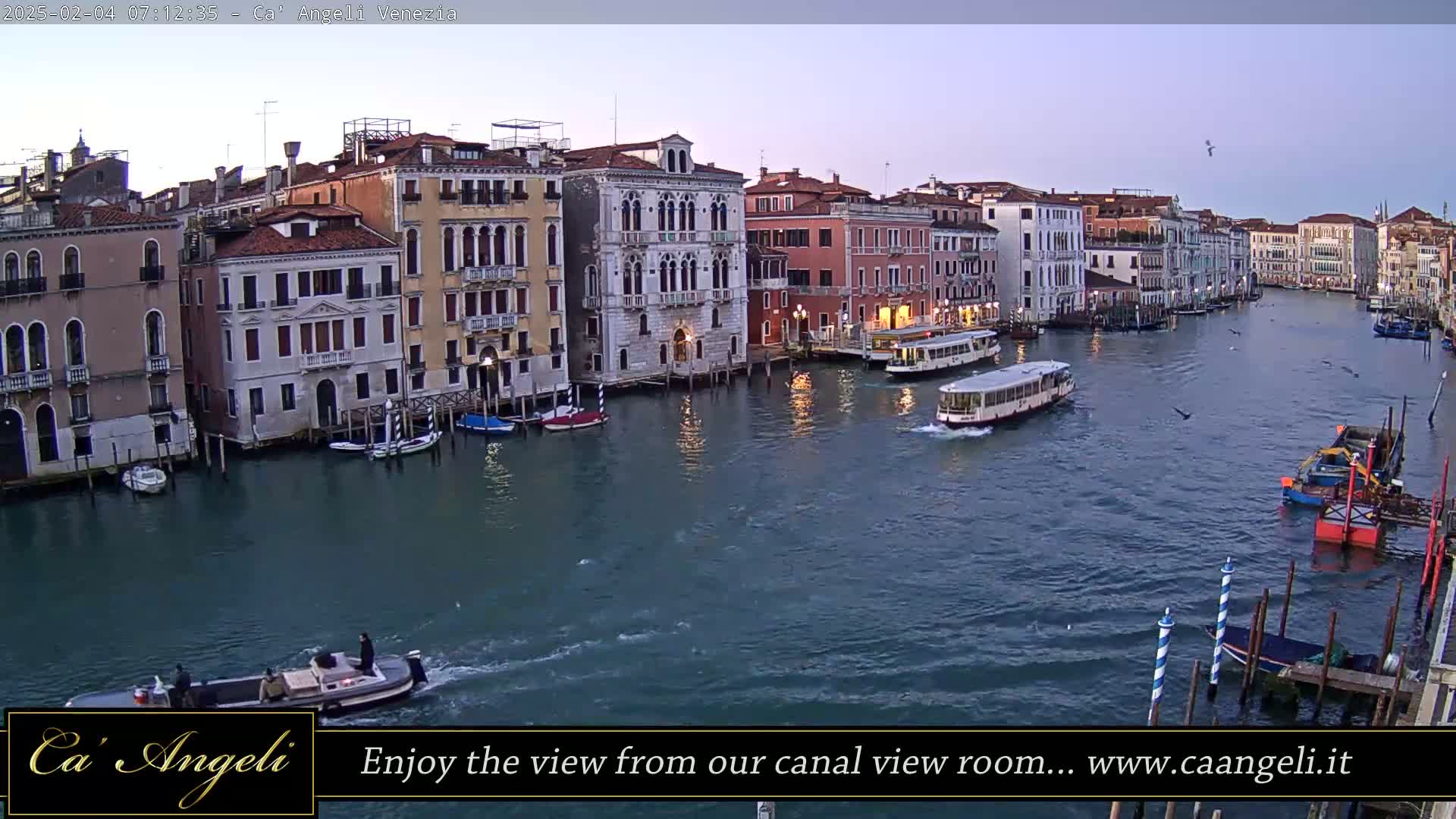 A wide shot shows a calm canal in Venice at dawn, lined with historic buildings and several boats, including a water bus.