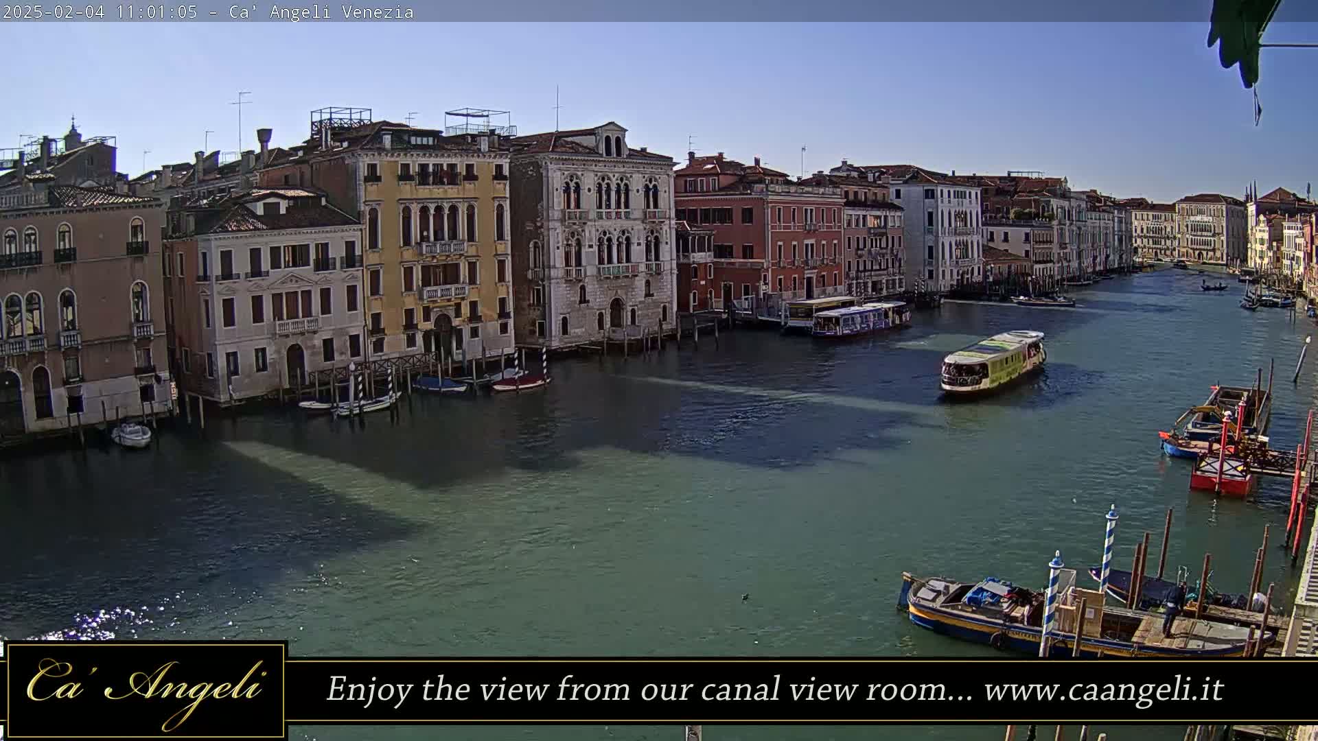 A sunny day in Venice shows a wide canal with several boats and buildings lining the waterway.