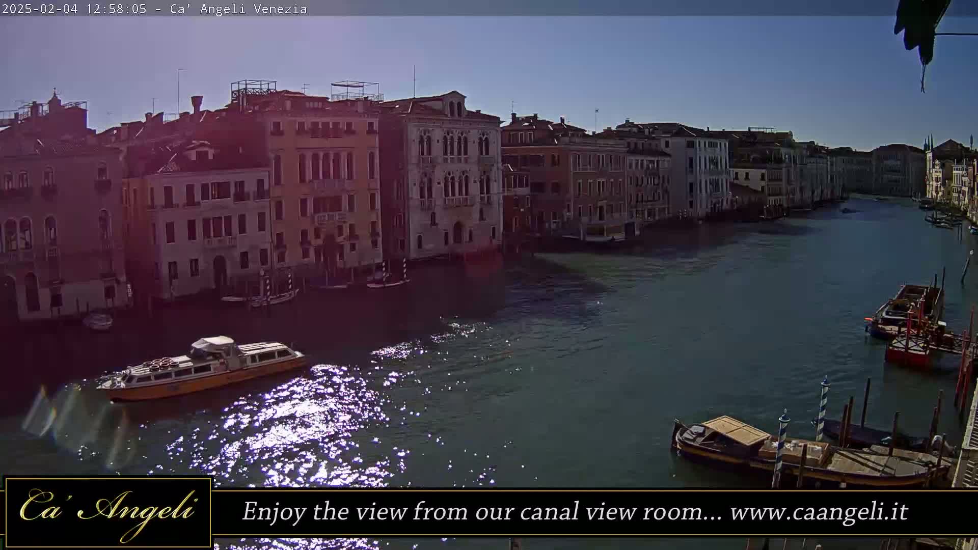 A sunny day shows a canal in Venice, Italy, with several boats and numerous buildings lining the waterway.