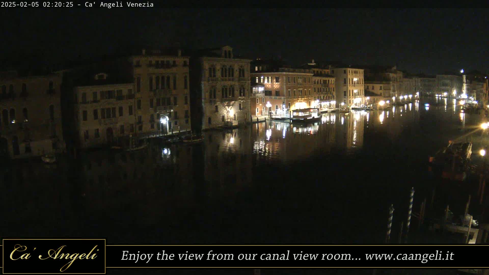 A nighttime view of a canal in Venice, with illuminated buildings lining the waterway, reflecting in the dark water.