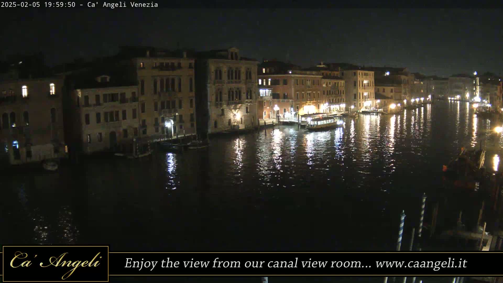 A nighttime view of a canal in Venice, Italy, showing illuminated buildings reflected in the dark water.