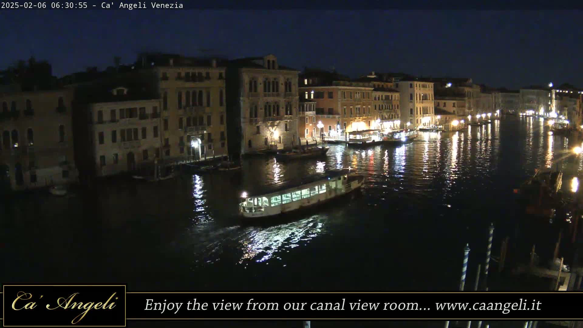 A nighttime view of a canal in Venice, showing illuminated buildings lining the waterway and a boat traveling on the dark water.