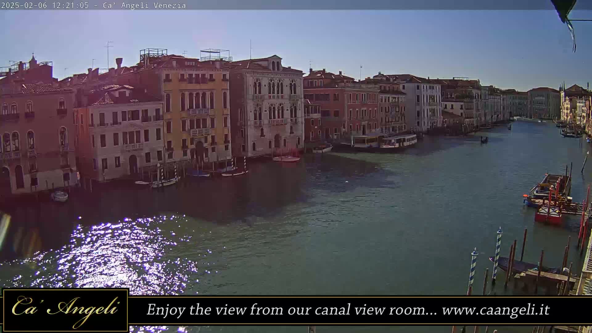 A sunny day in Venice shows a wide canal lined with buildings, boats, and gondolas.