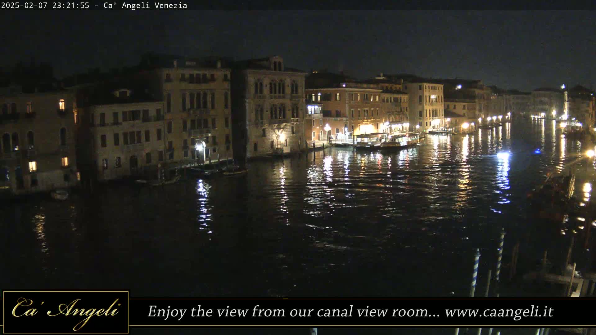 A nighttime view of a canal in Venice, Italy, shows illuminated buildings reflected in the dark water.