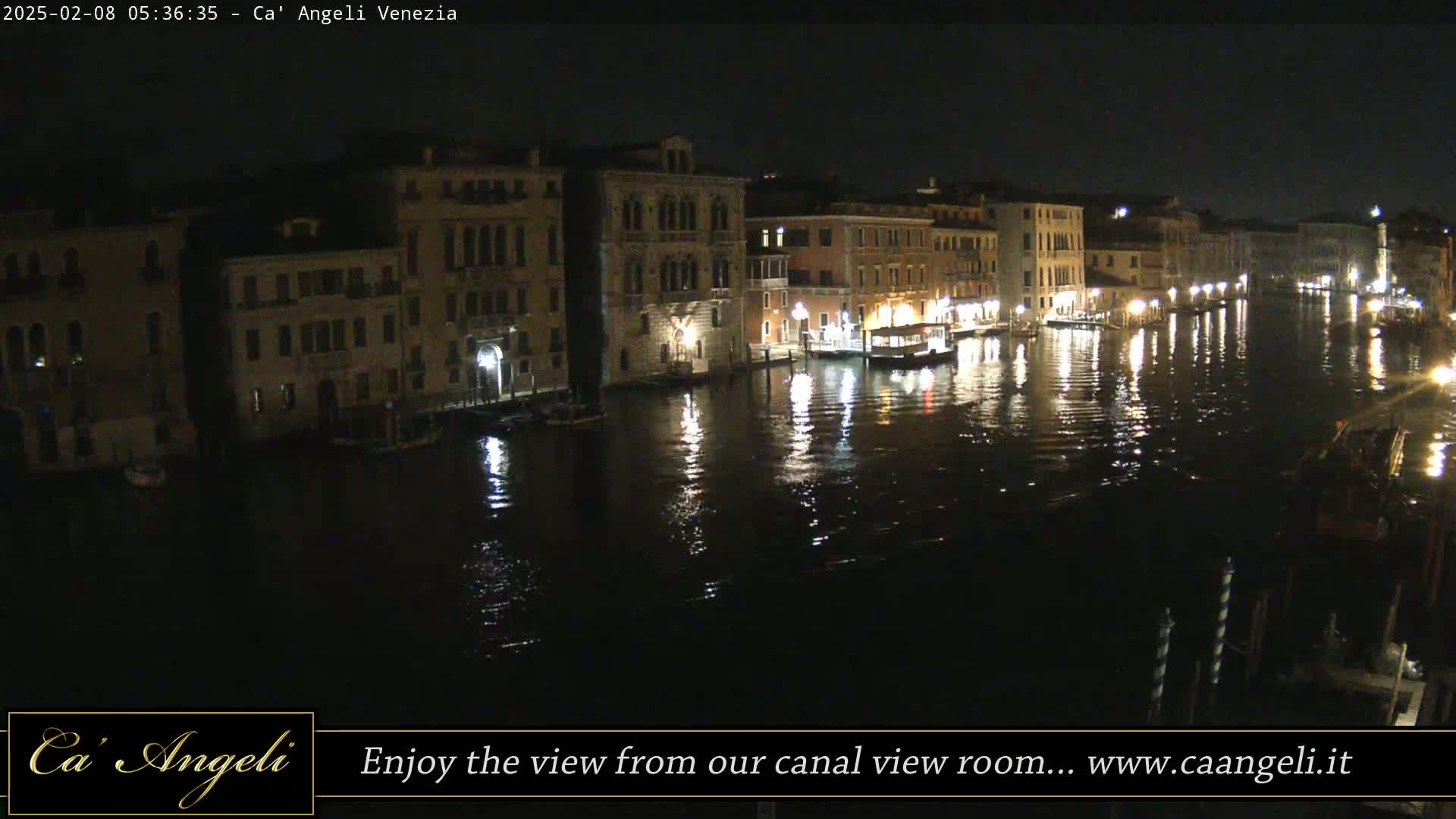 A nighttime view of a canal in Venice, with illuminated buildings lining the waterway and their lights reflecting on the dark water.