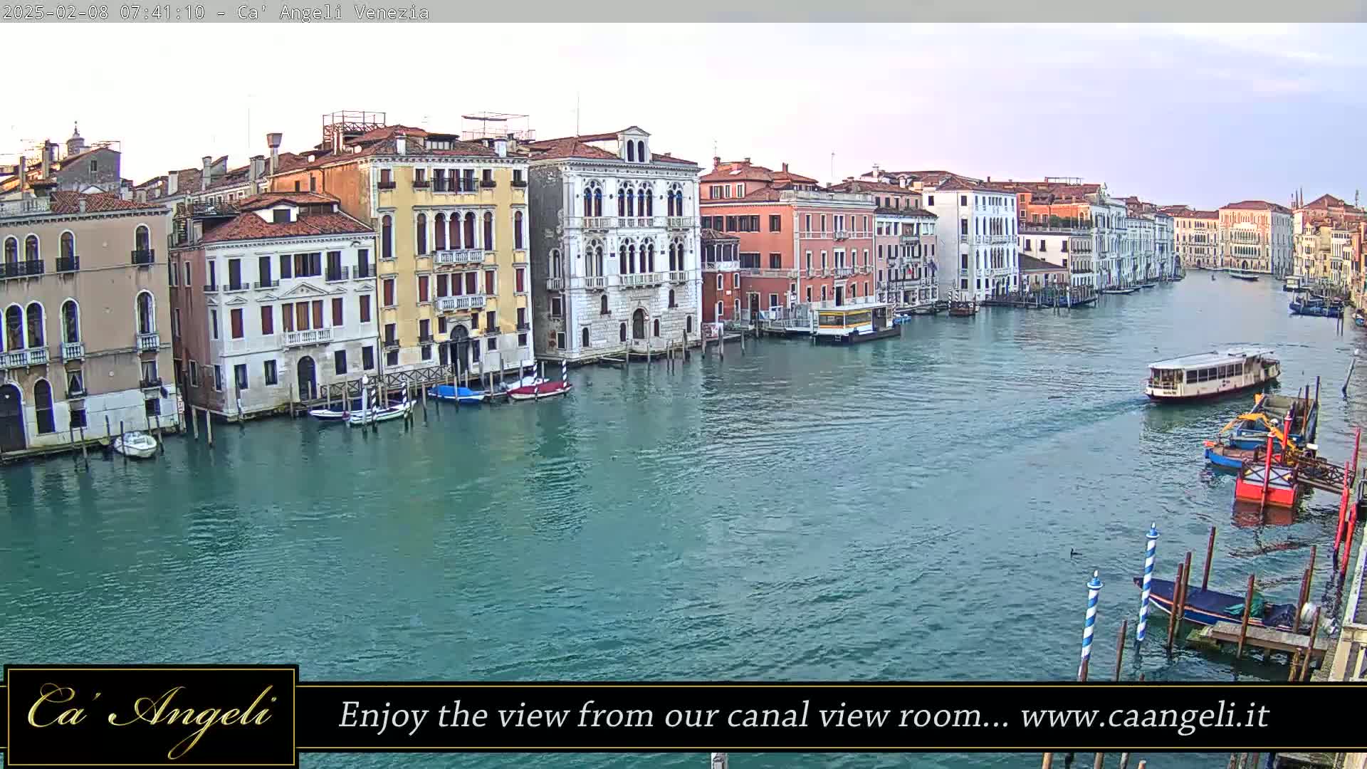 A waterway with several boats and numerous buildings along its banks under a partly cloudy sky.