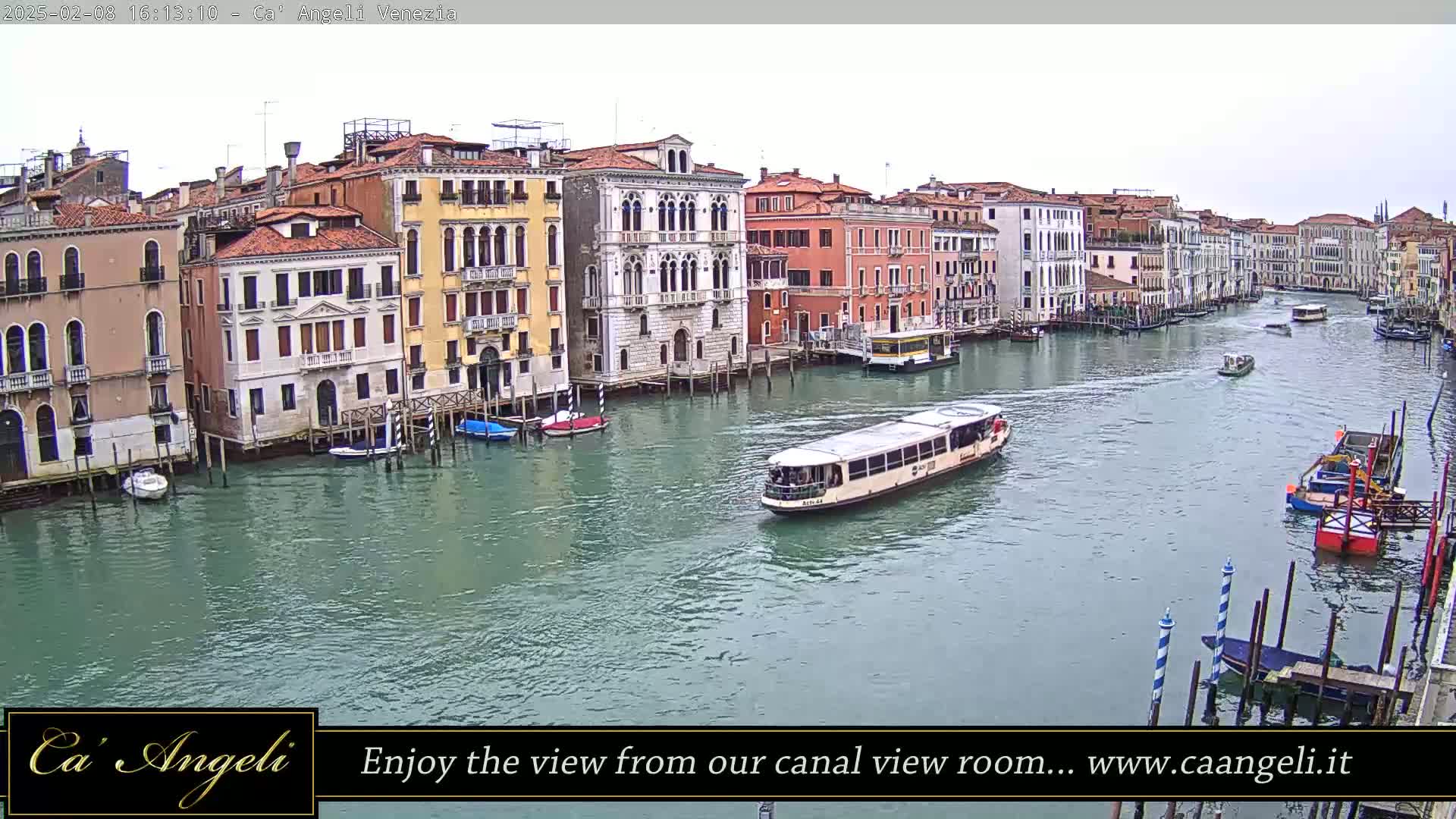 A waterway in Venice, Italy, shows several boats and buildings along its banks under an overcast sky.