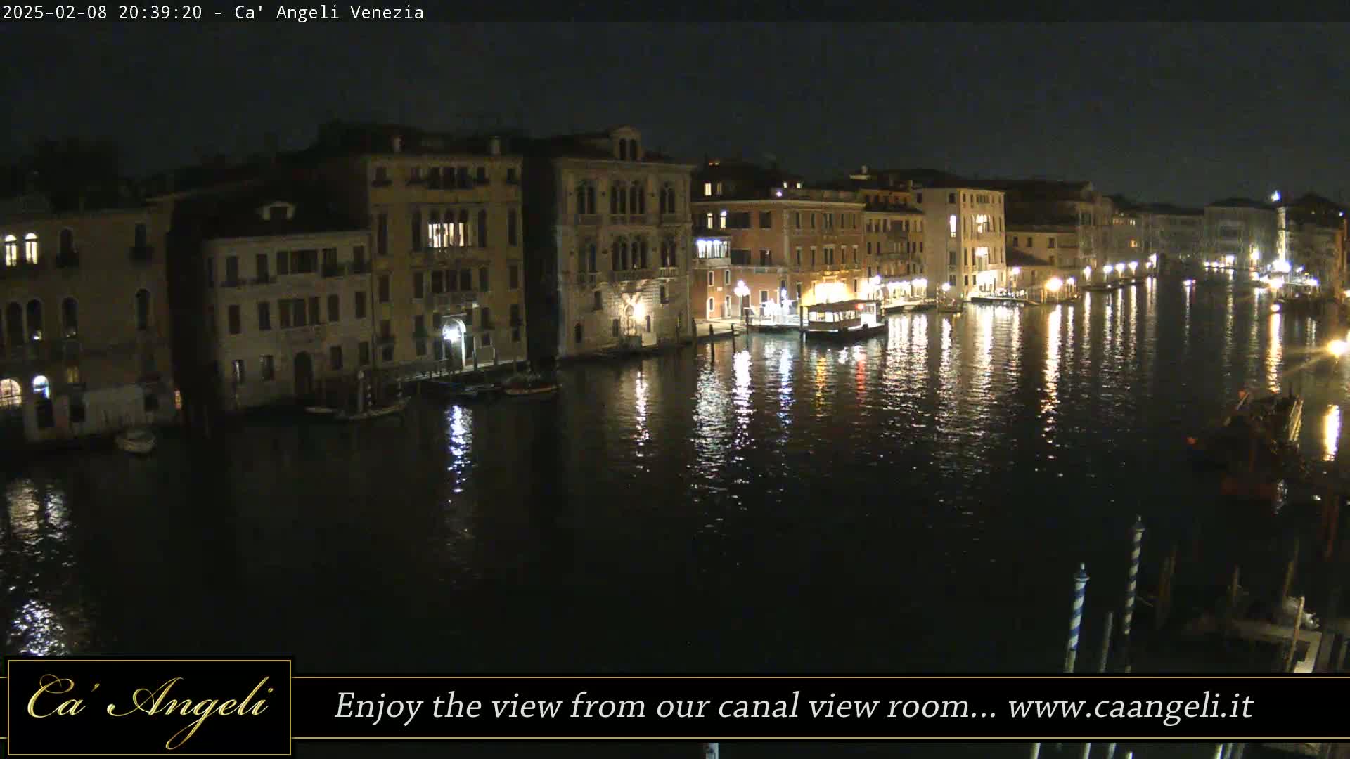 A nighttime view of a canal in Venice, Italy, shows illuminated buildings lining the waterway, reflected in the dark water.