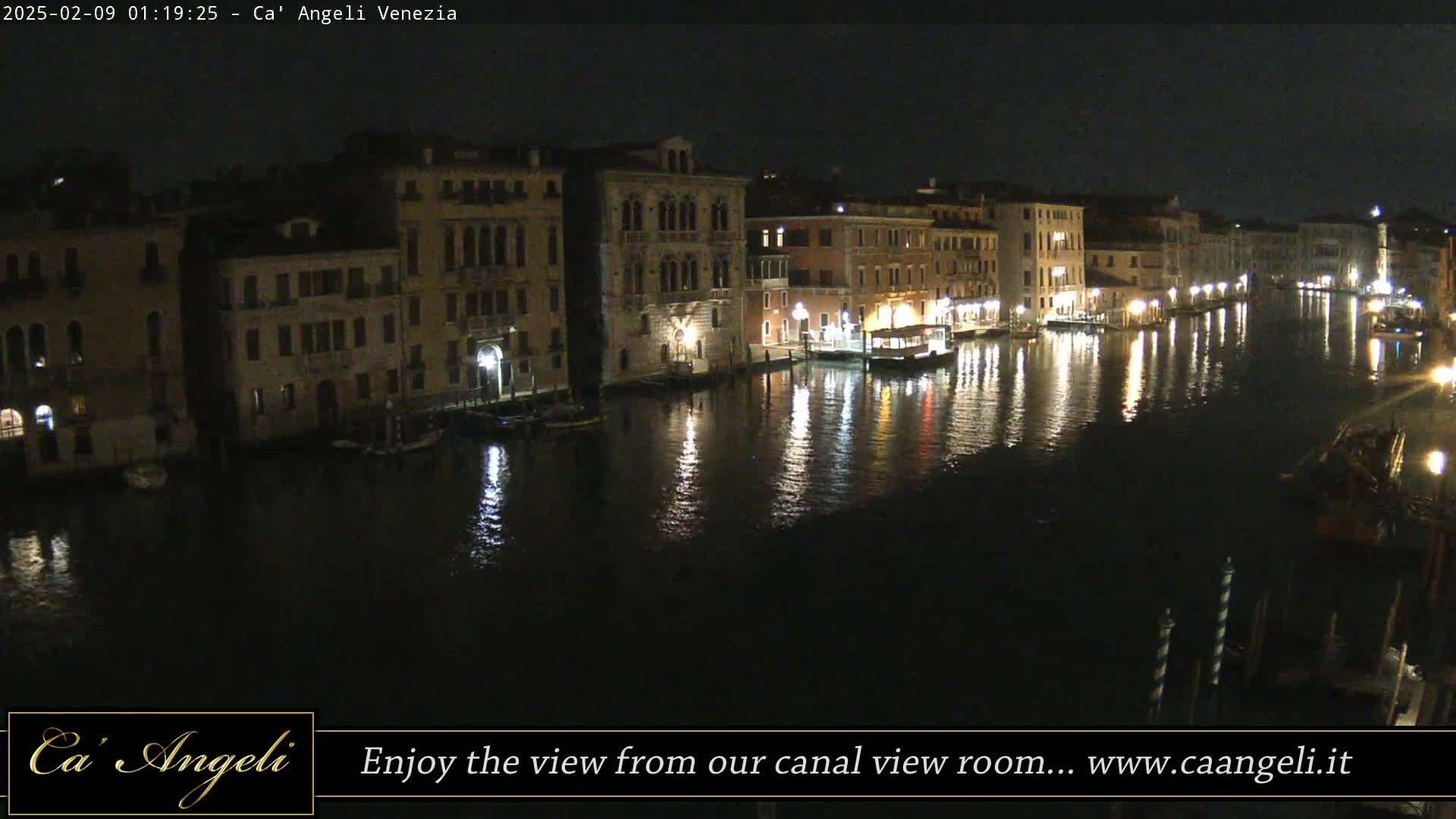 A nighttime view of a canal in Venice, Italy, shows buildings lit by lights reflected on the dark water.