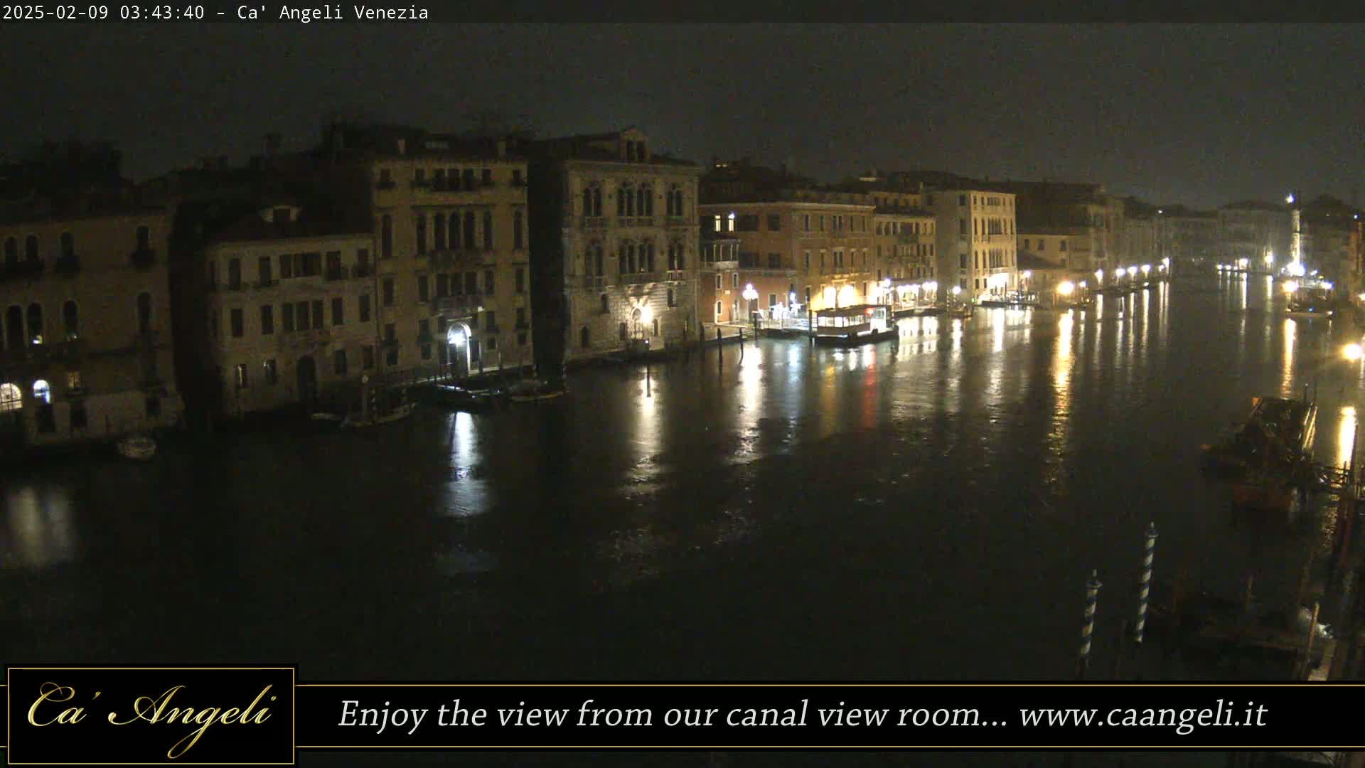 A nighttime view of a canal in Venice, with illuminated buildings lining the waterway under a dark sky.