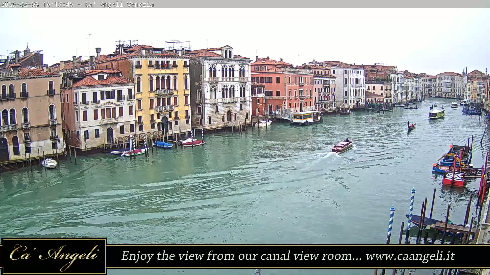 A wide shot of a canal in Venice, Italy, on an overcast day shows numerous boats and buildings lining the waterway.