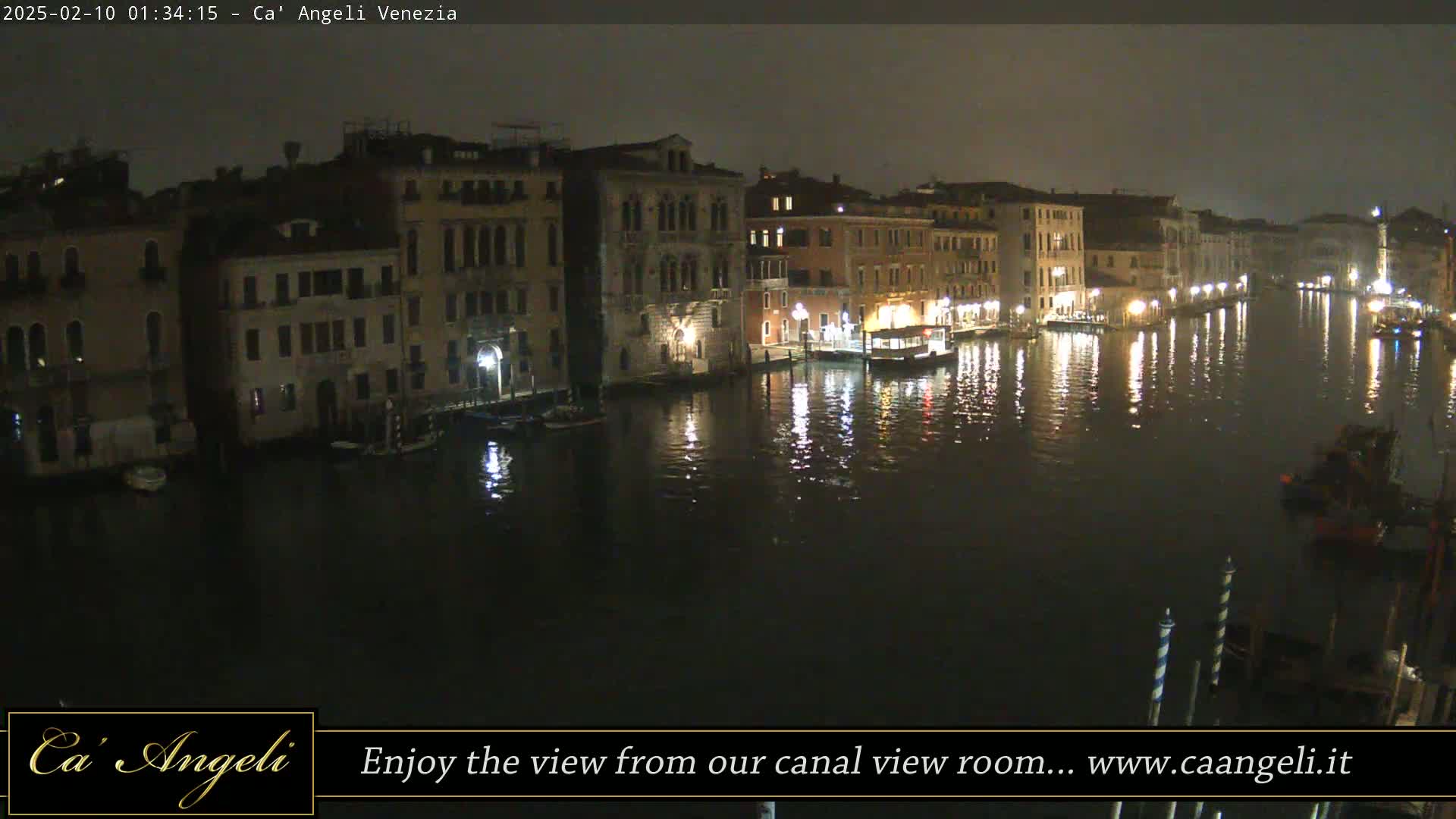 A nighttime view of a canal in Venice, Italy, with illuminated buildings lining the waterway, reflecting in the dark water under a dark sky.
