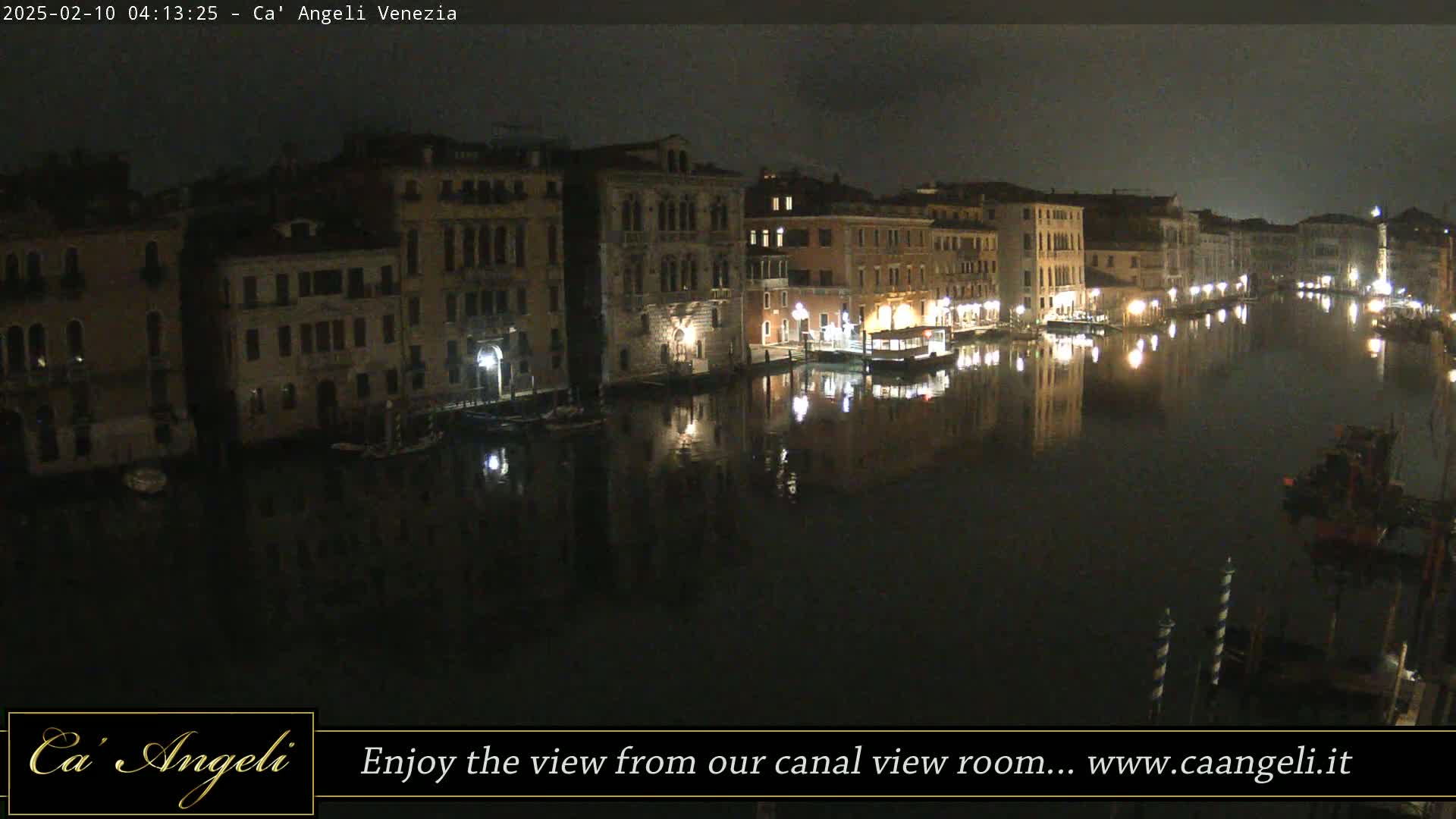 A nighttime view of a calm canal in Venice, lined with illuminated buildings reflecting in the dark water.