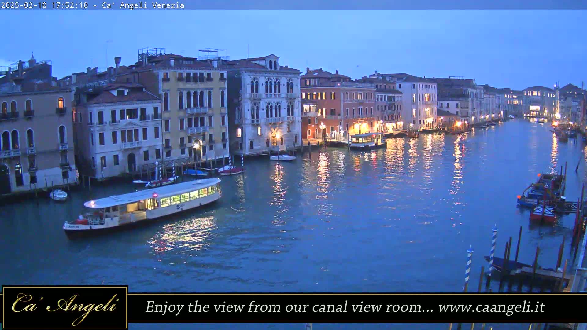 A wide canal in Venice at twilight, lined with illuminated buildings and several boats, including a passenger ferry.