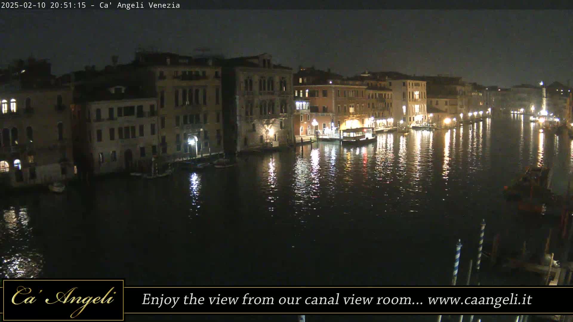 A nighttime view of a canal in Venice, showing illuminated buildings lining the waterway and their reflections in the dark water.