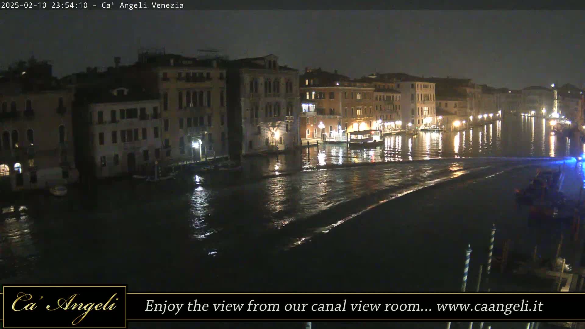 A nighttime view of a canal in Venice, showing illuminated buildings lining the waterway, with a boat moving on the water.
