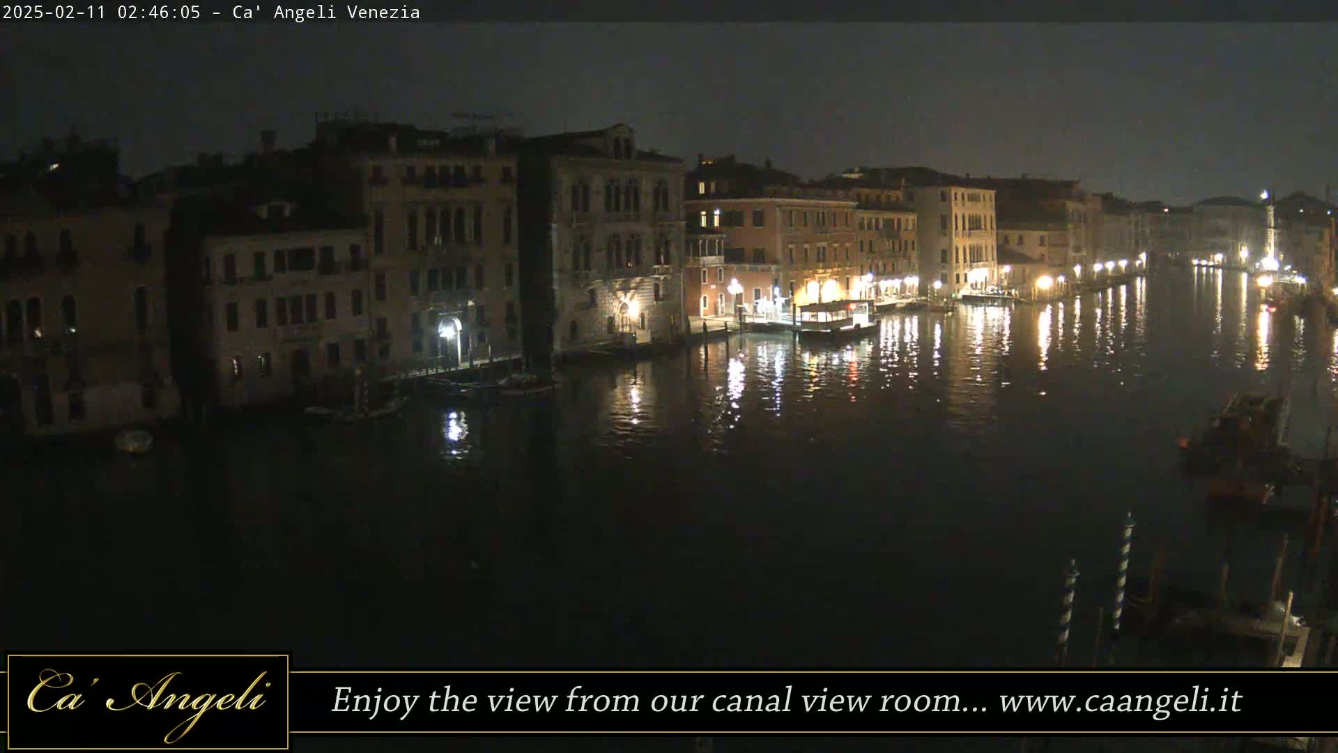 A nighttime view of a calm canal in Venice, lined with illuminated buildings.