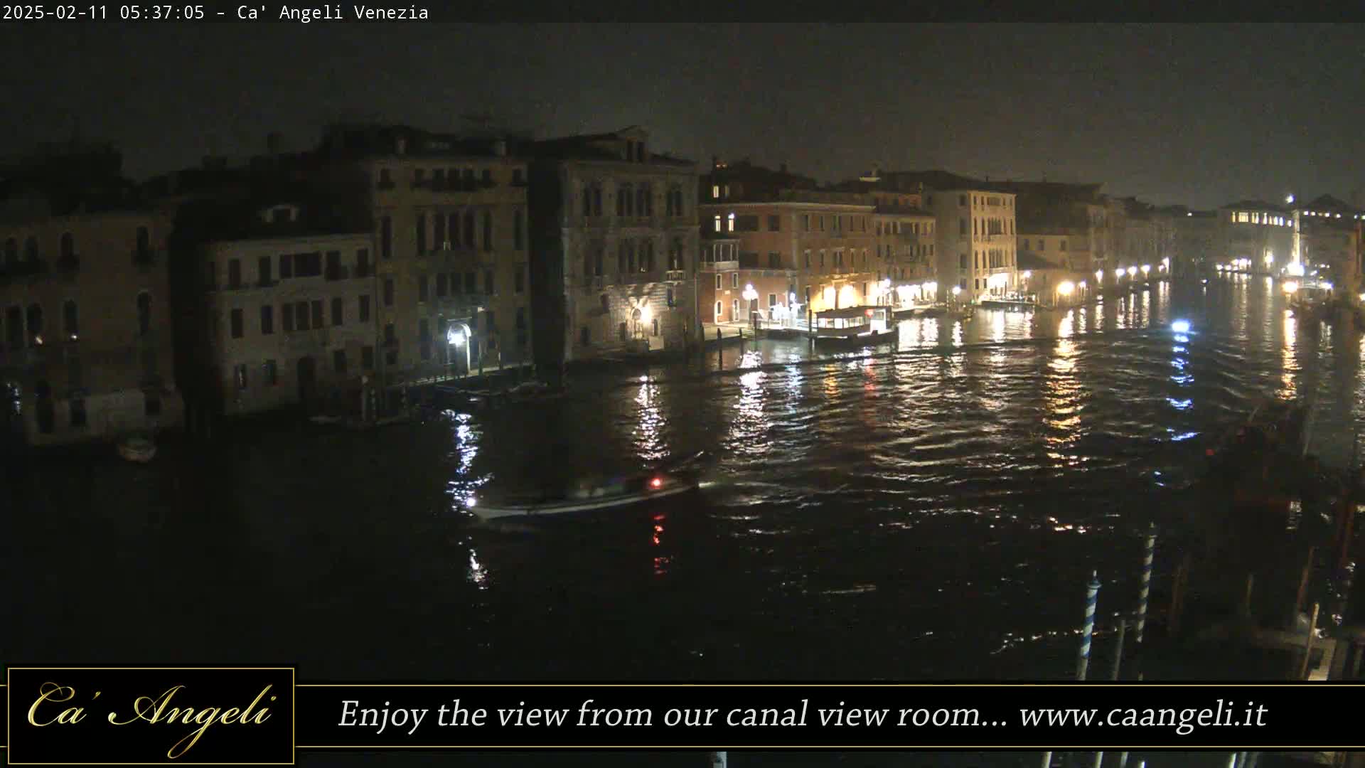 A nighttime view of a canal in Venice, with several buildings illuminated along the waterway, and a small boat moving on the water.