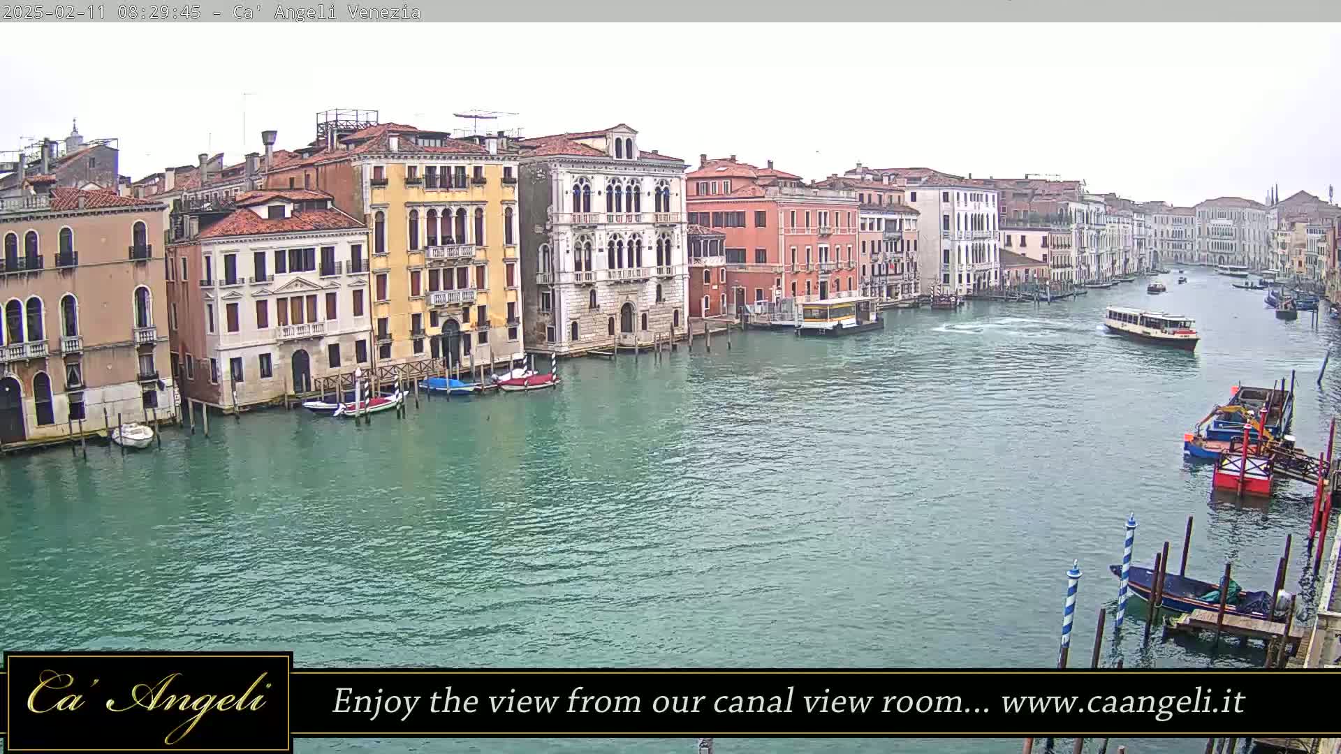 A wide shot of a canal in Venice, Italy on an overcast day, shows several colorful buildings lining the waterway, with boats and watercraft traveling along the canal.