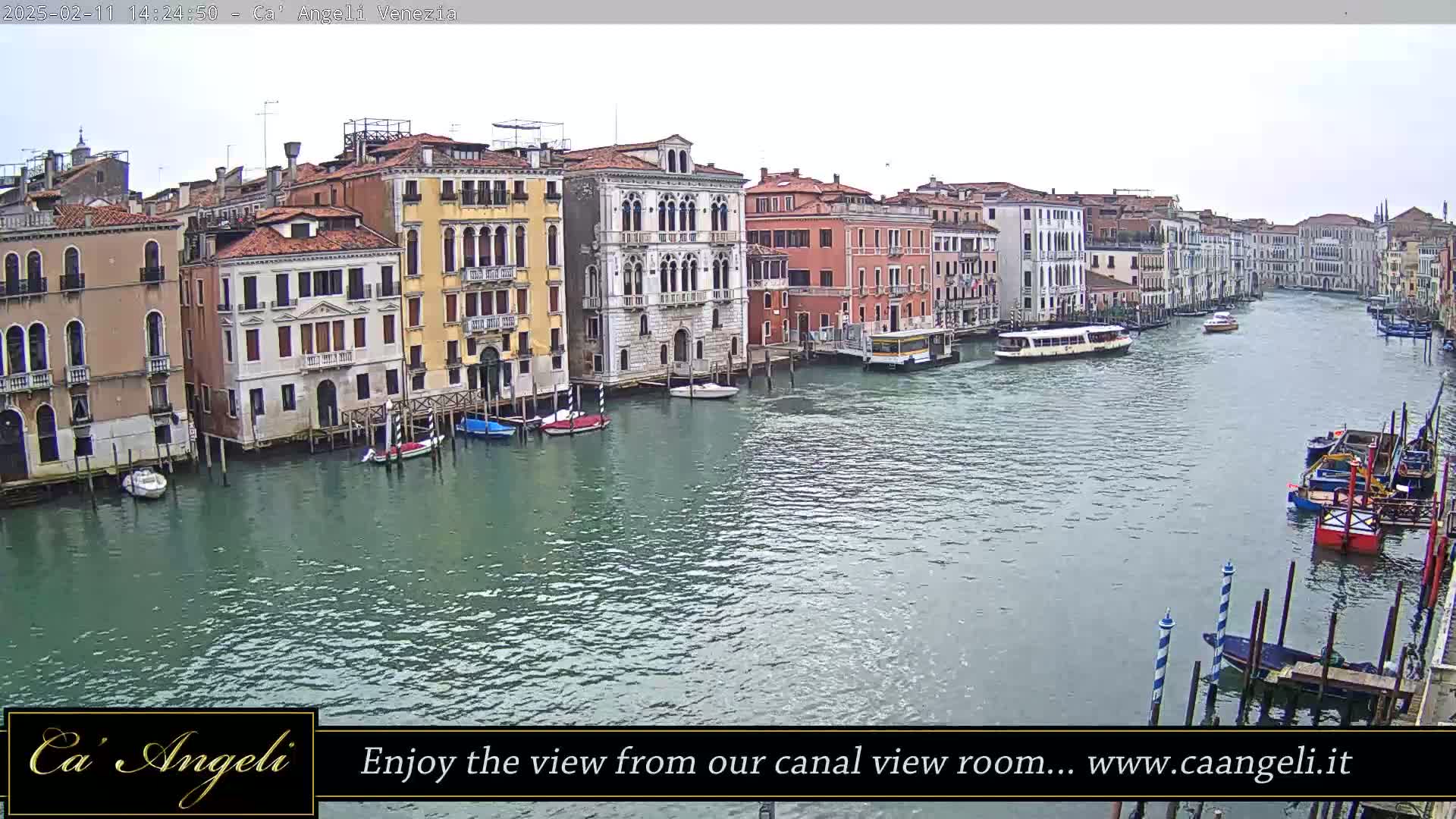 A wide shot shows a calm canal in Venice, Italy, with numerous boats and buildings lining the waterway under an overcast sky.