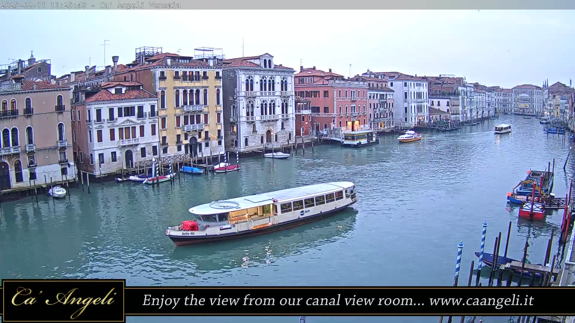 A waterway in Venice, Italy, shows several buildings lining the canal, with a passenger boat on the water under an overcast sky.