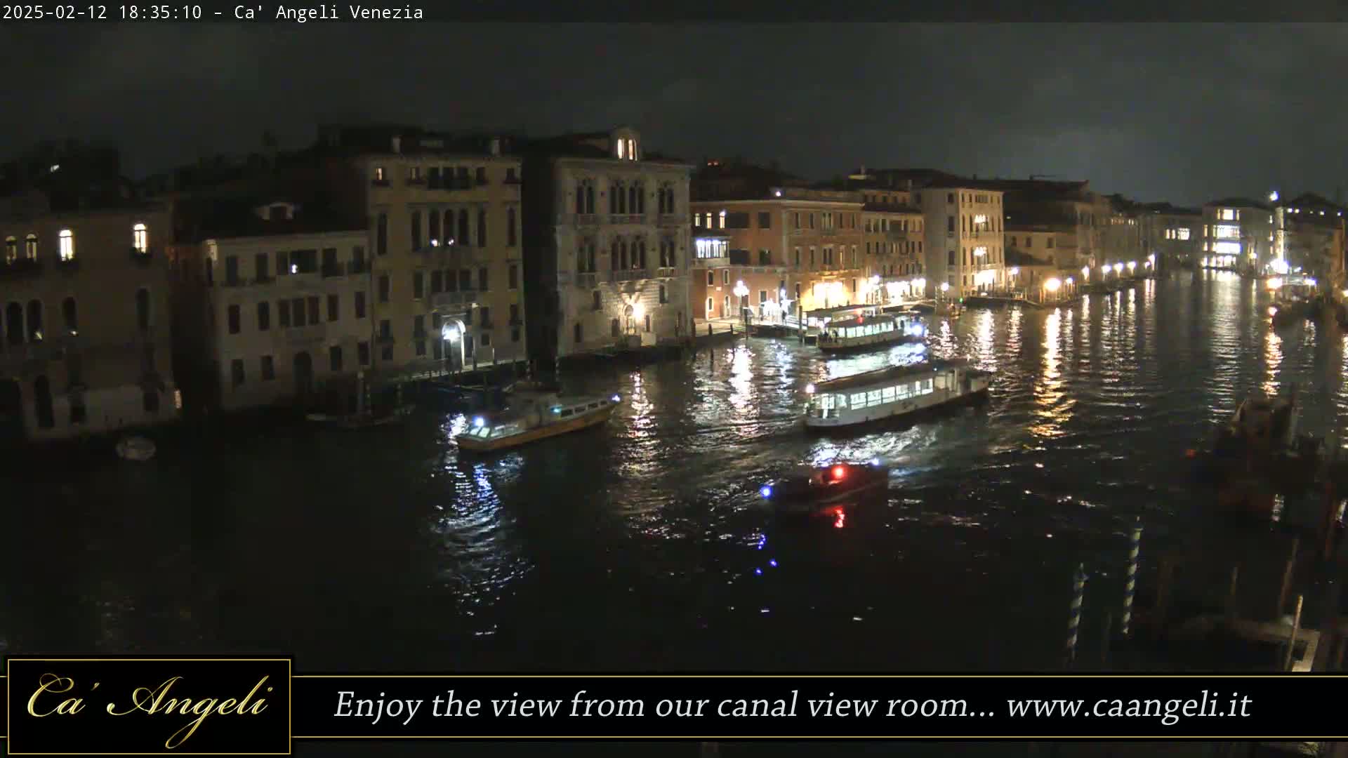 A nighttime view of a canal in Venice, with several boats and illuminated buildings lining the waterway.