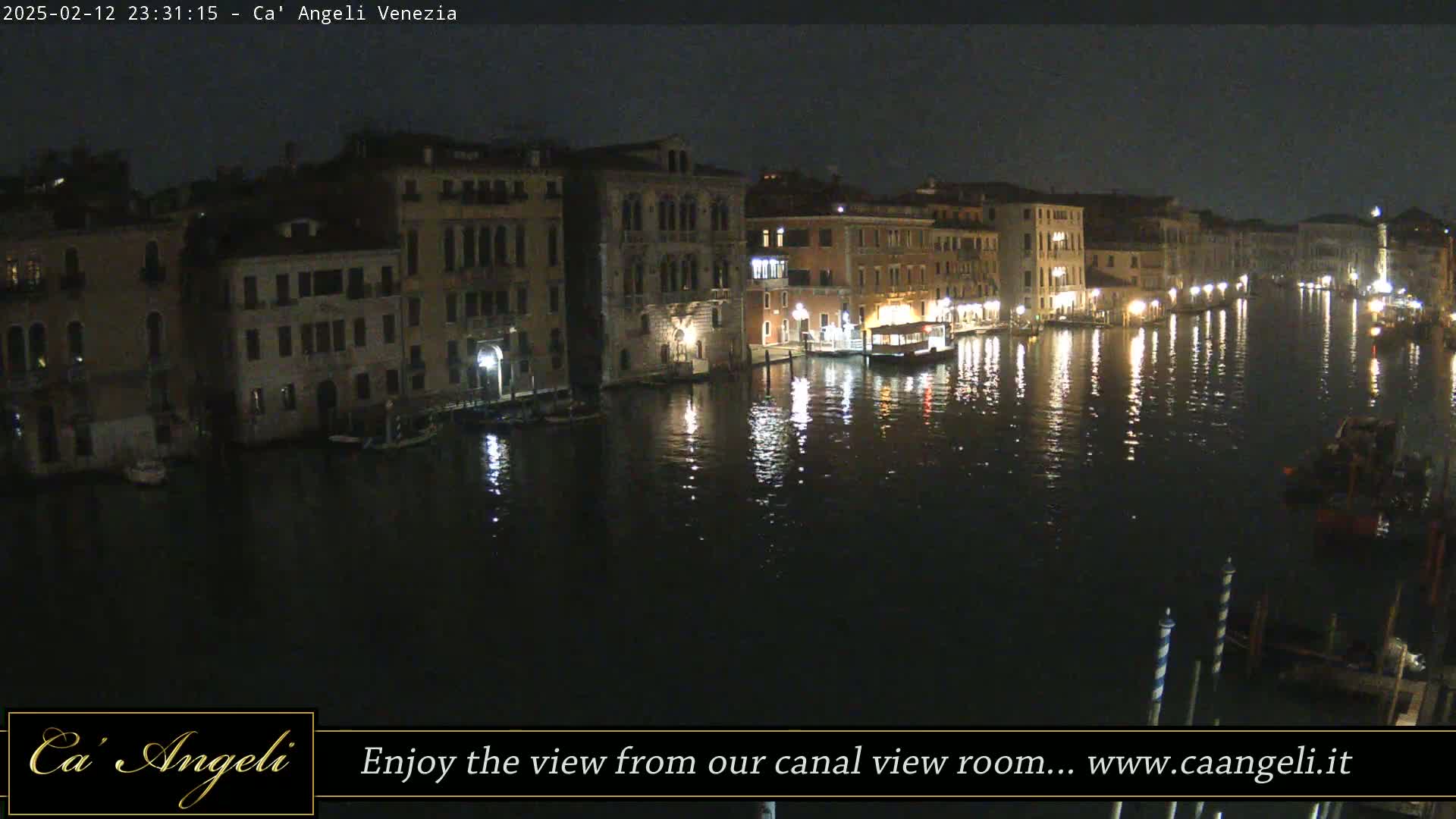 A nighttime view of a canal in Venice, Italy, with illuminated buildings lining its banks and their lights reflecting on the dark water.