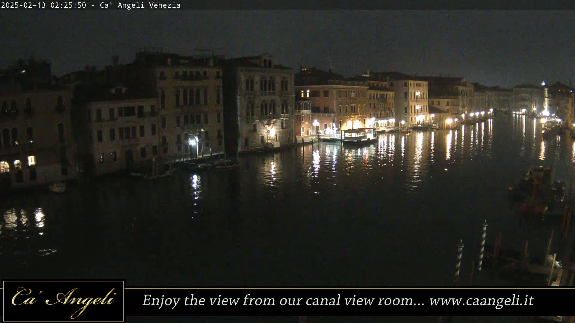 A nighttime view of a canal in Venice, with lights reflecting on the dark water and illuminated buildings lining the waterway.