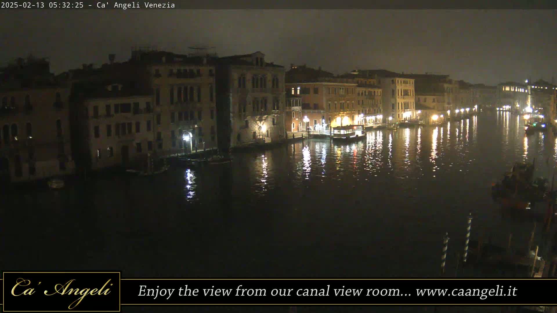 A nighttime view of a canal in Venice, Italy, with illuminated buildings lining the waterway and their reflections shimmering on the dark water.