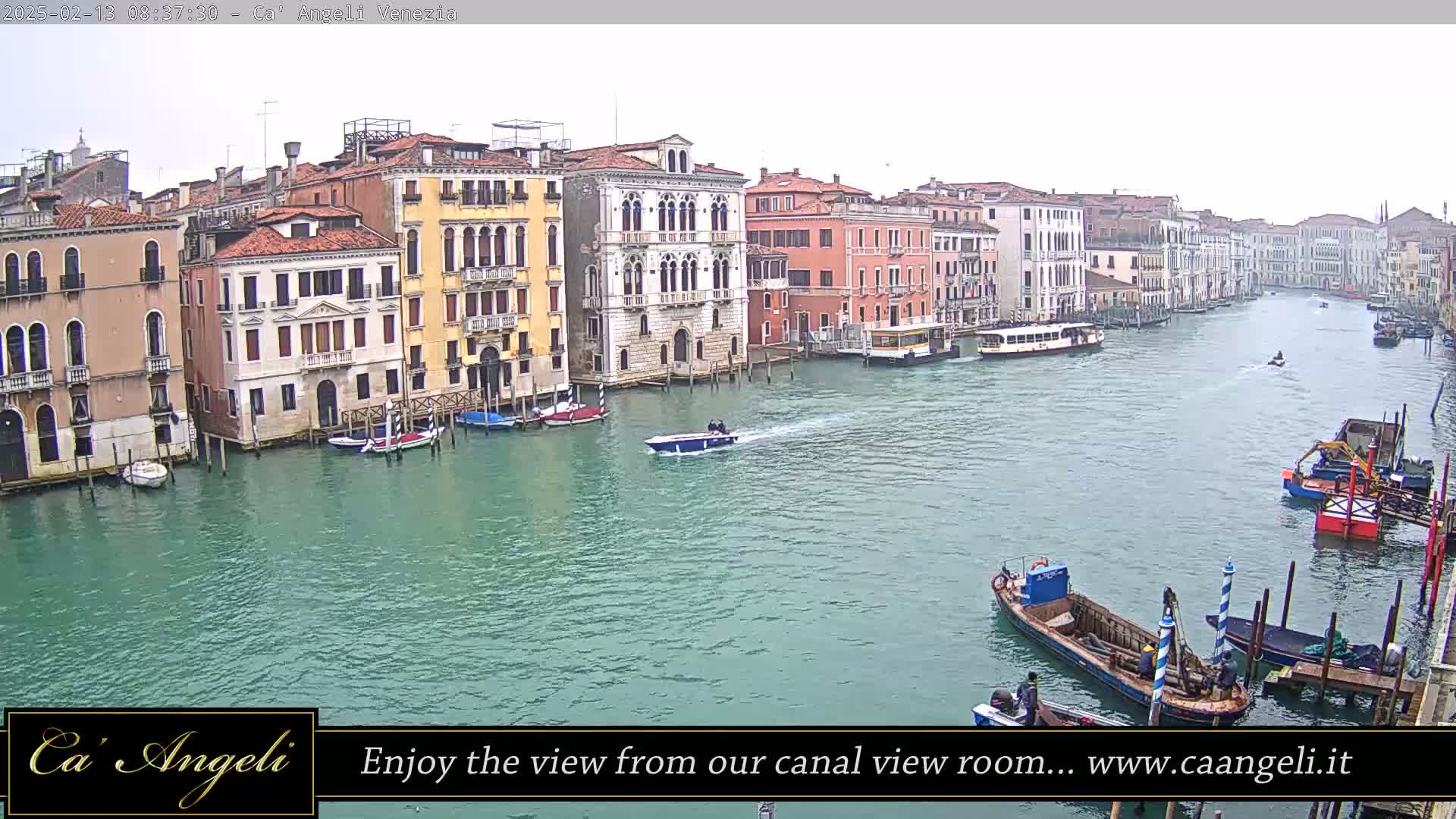 A wide shot of a Venetian canal on an overcast day shows numerous boats and colorful buildings lining the waterway.